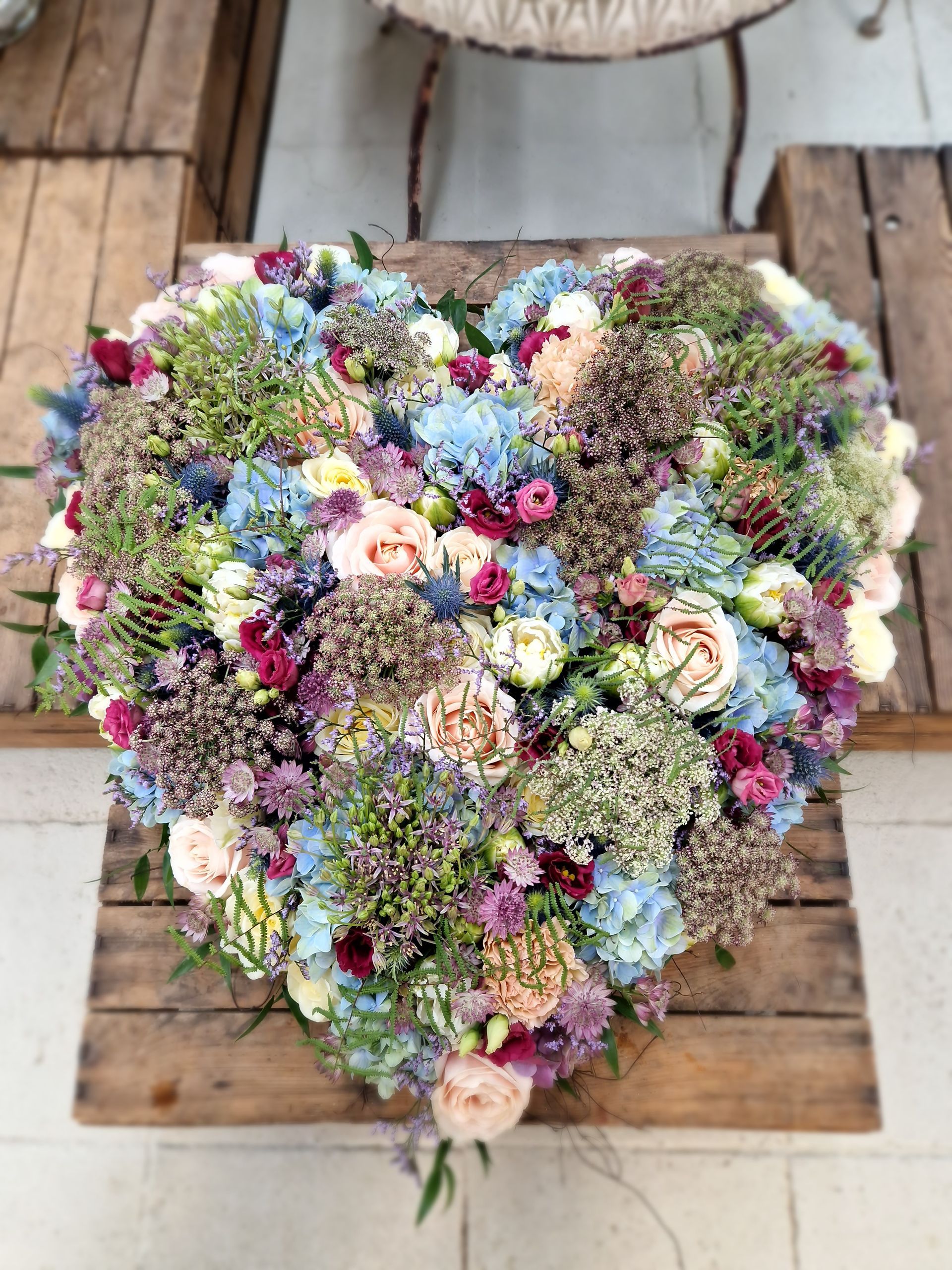 Ein herzförmiger Blumenstrauß steht auf einem Holztisch.
