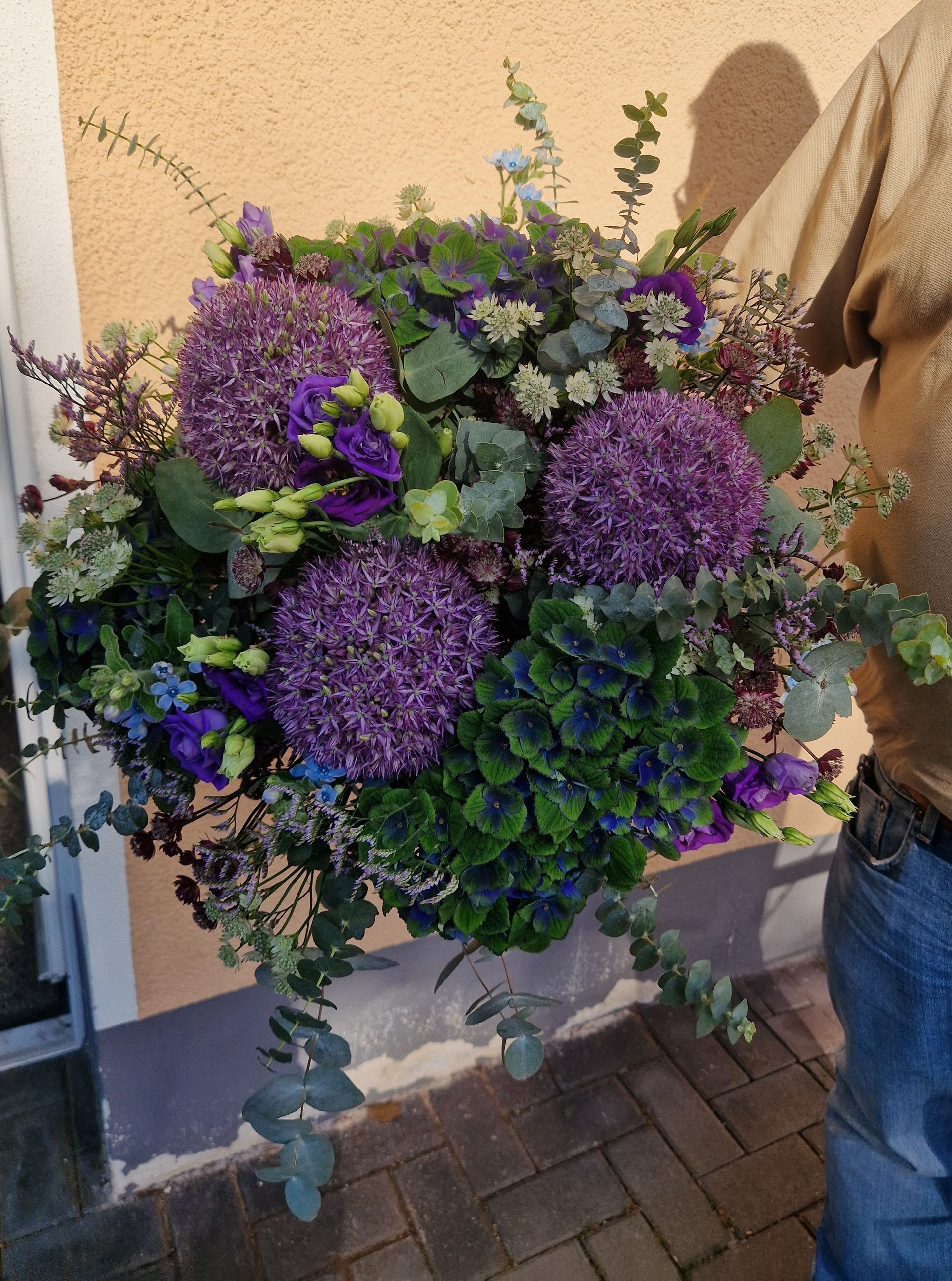 Ein Mann hält einen großen Strauß lila und grüner Blumen