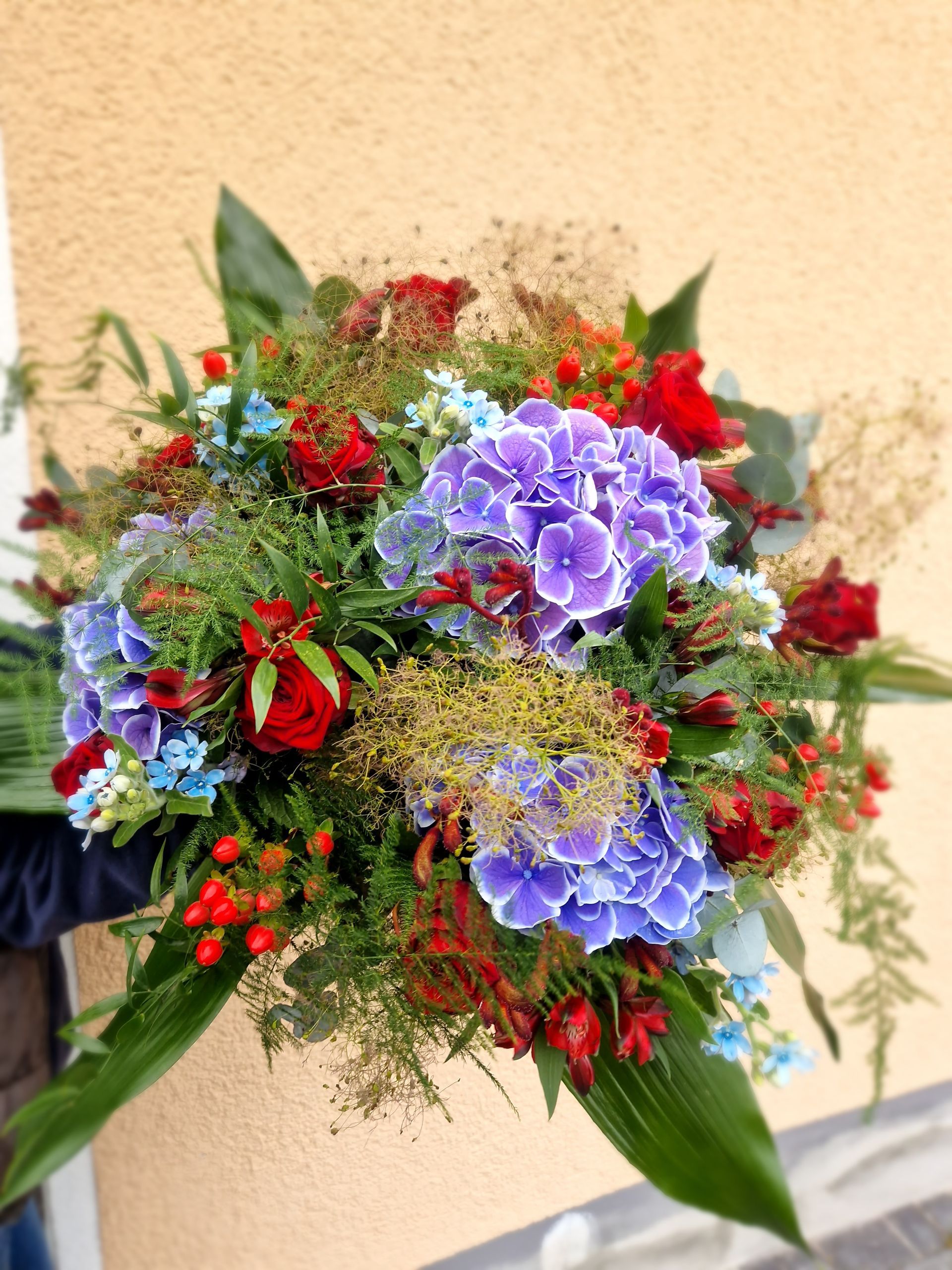 Eine Person hält einen Strauß blauer und roter Blumen