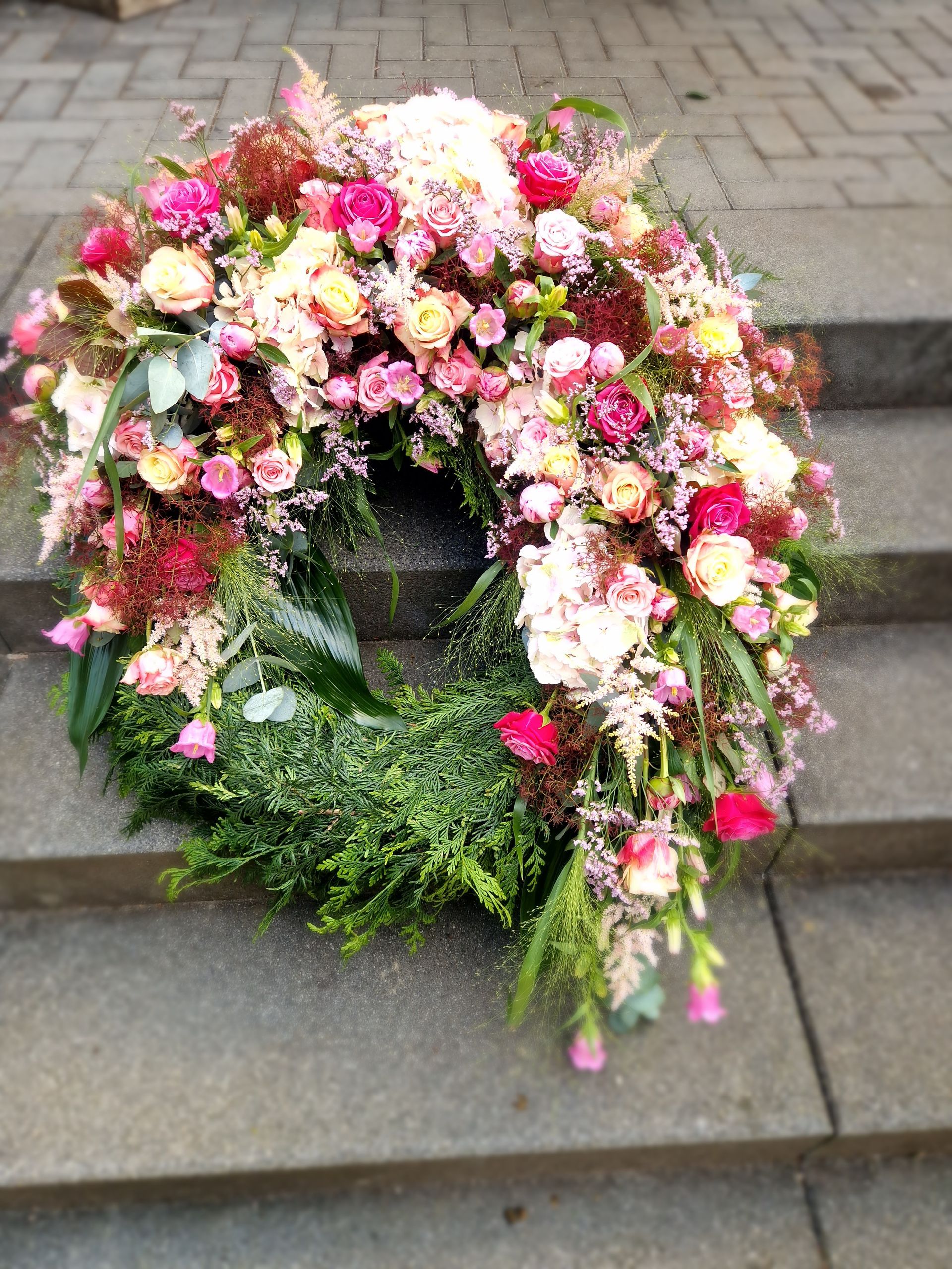 Auf einer Treppe steht ein Kranz aus rosa und gelben Blumen.