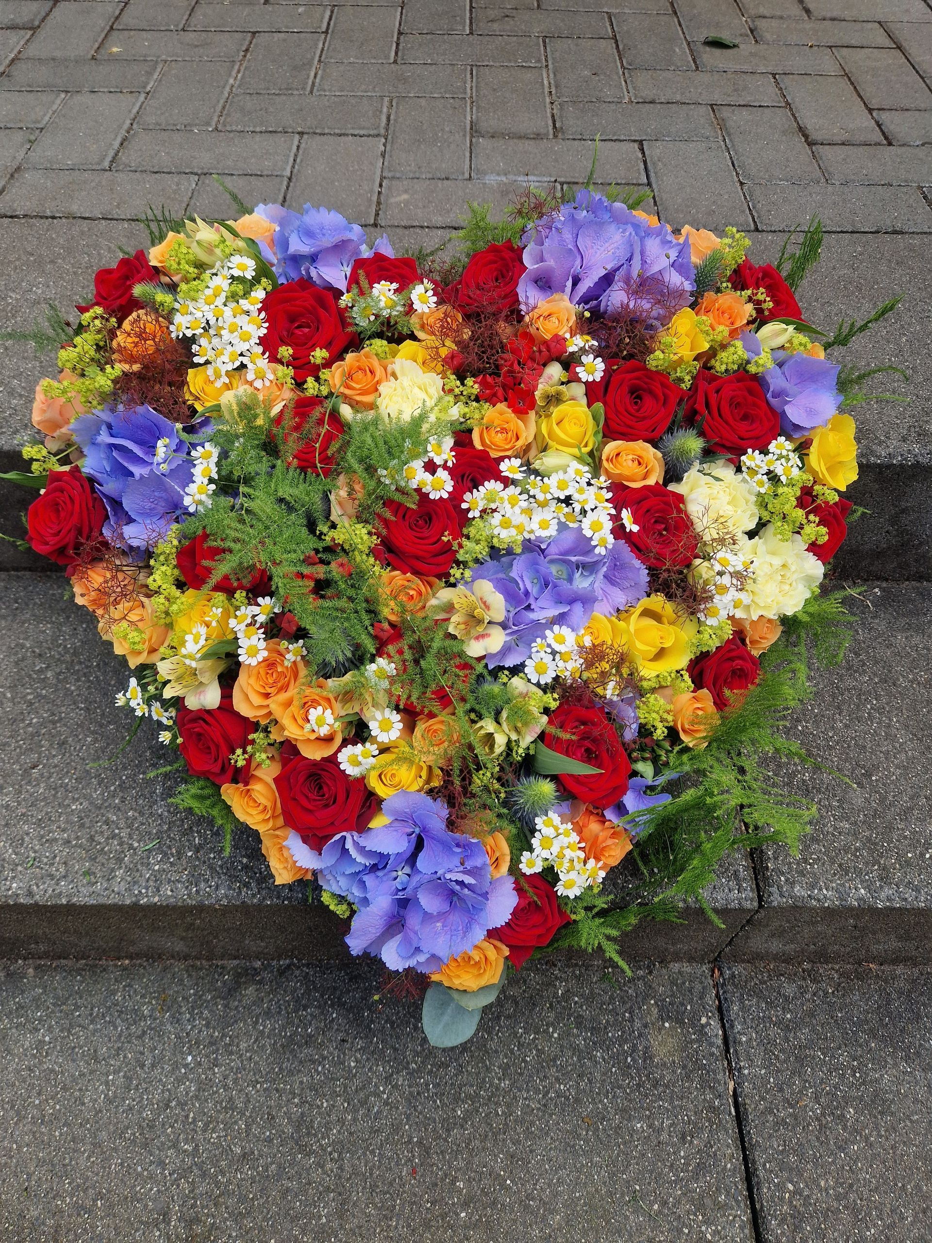 Auf einem Bürgersteig steht ein herzförmiger Blumenstrauß.
