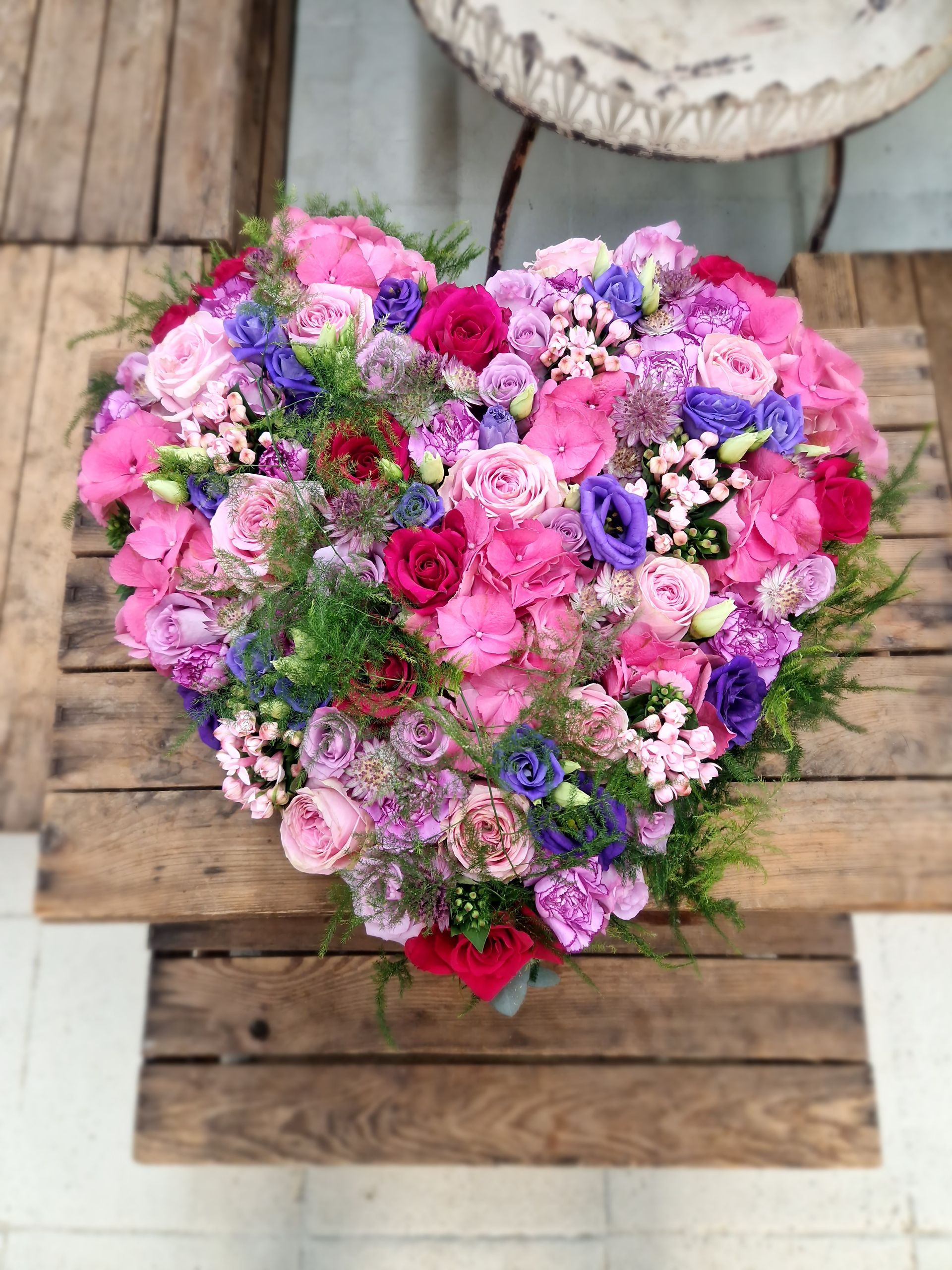 Ein herzförmiges Arrangement aus rosa und lila Blumen auf einem Holztisch