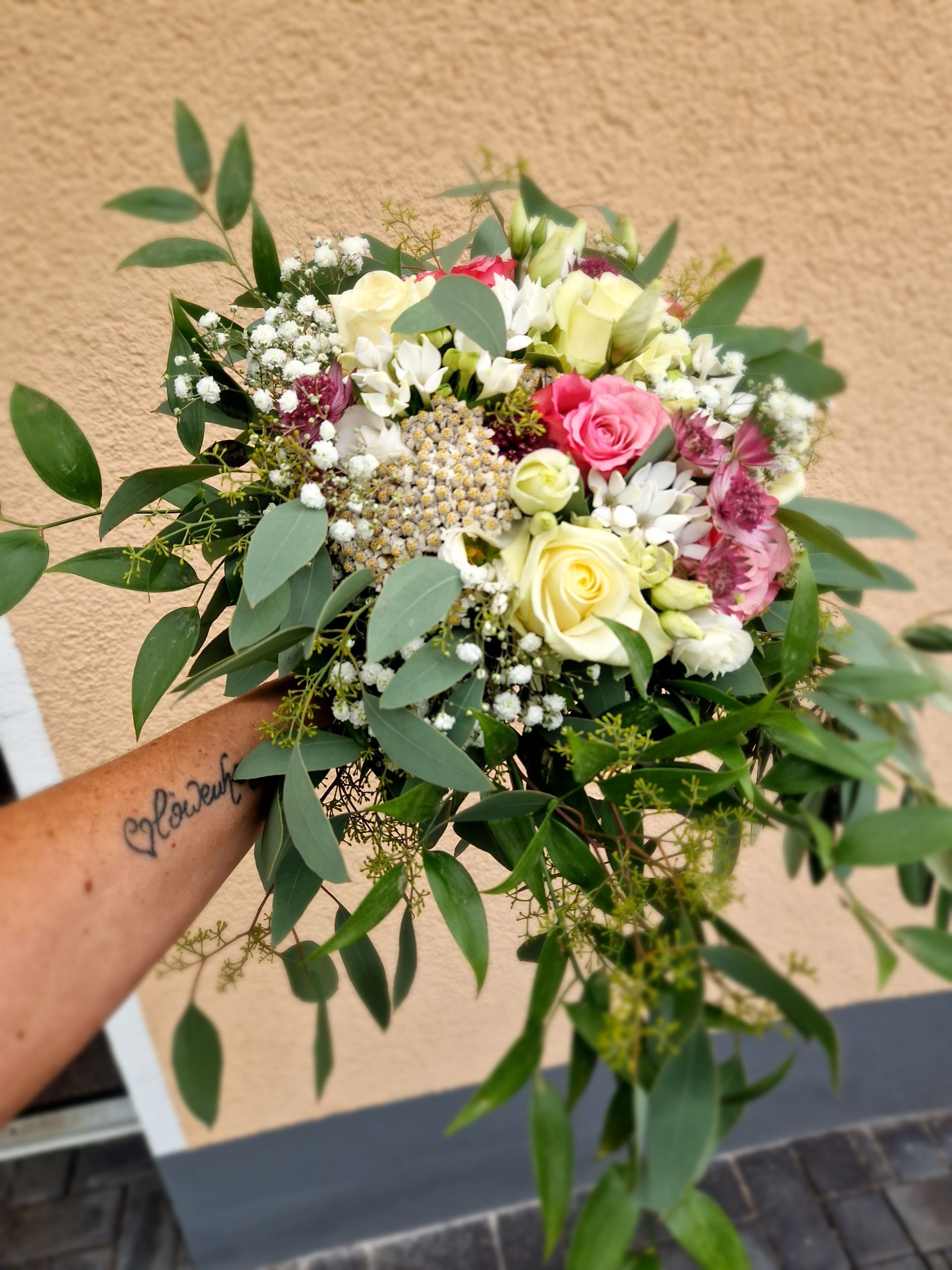 Eine Person mit einer Tätowierung auf dem Arm hält einen Blumenstrauß