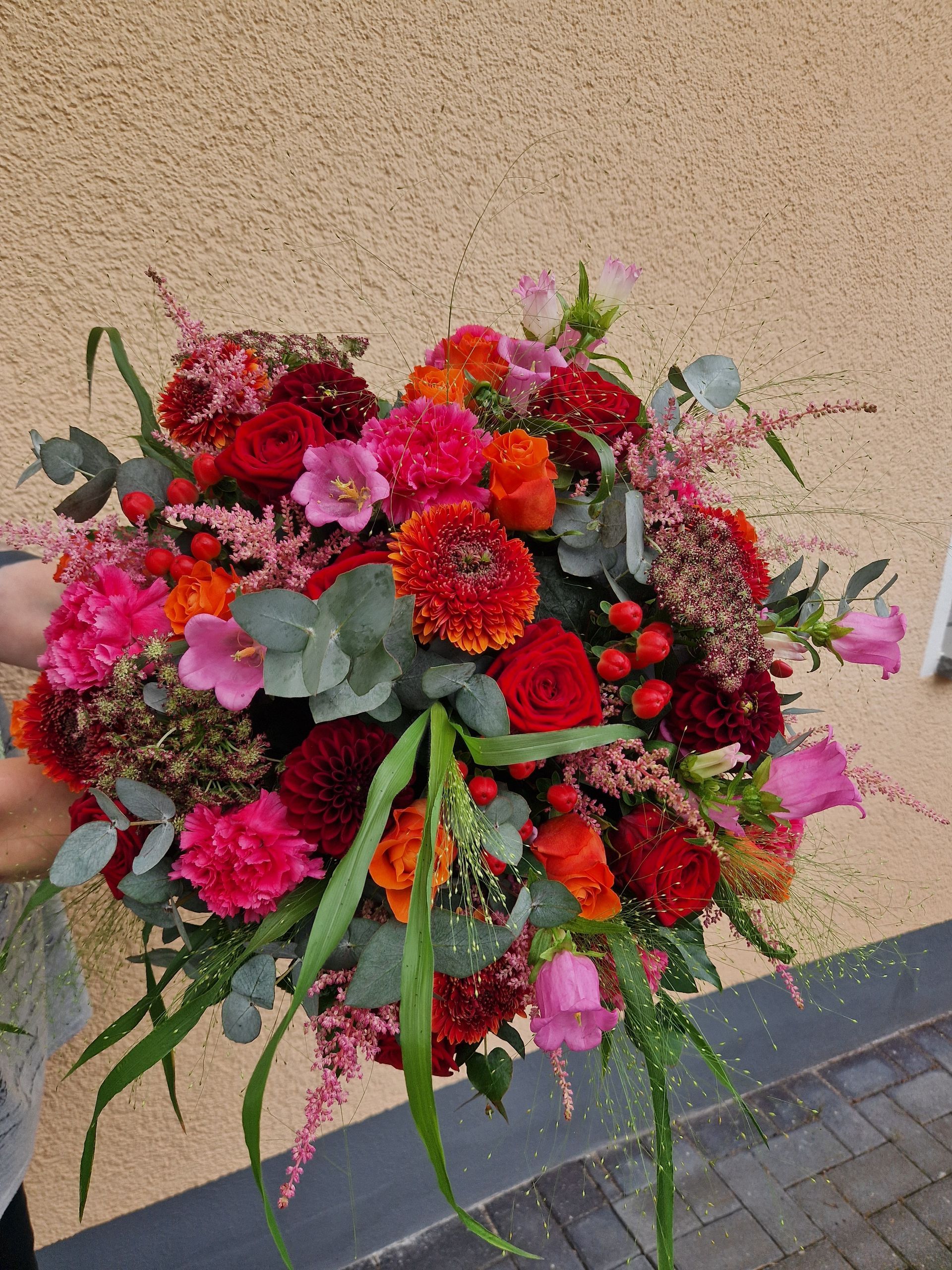 Eine Person hält einen großen Blumenstrauß vor einem Gebäude.