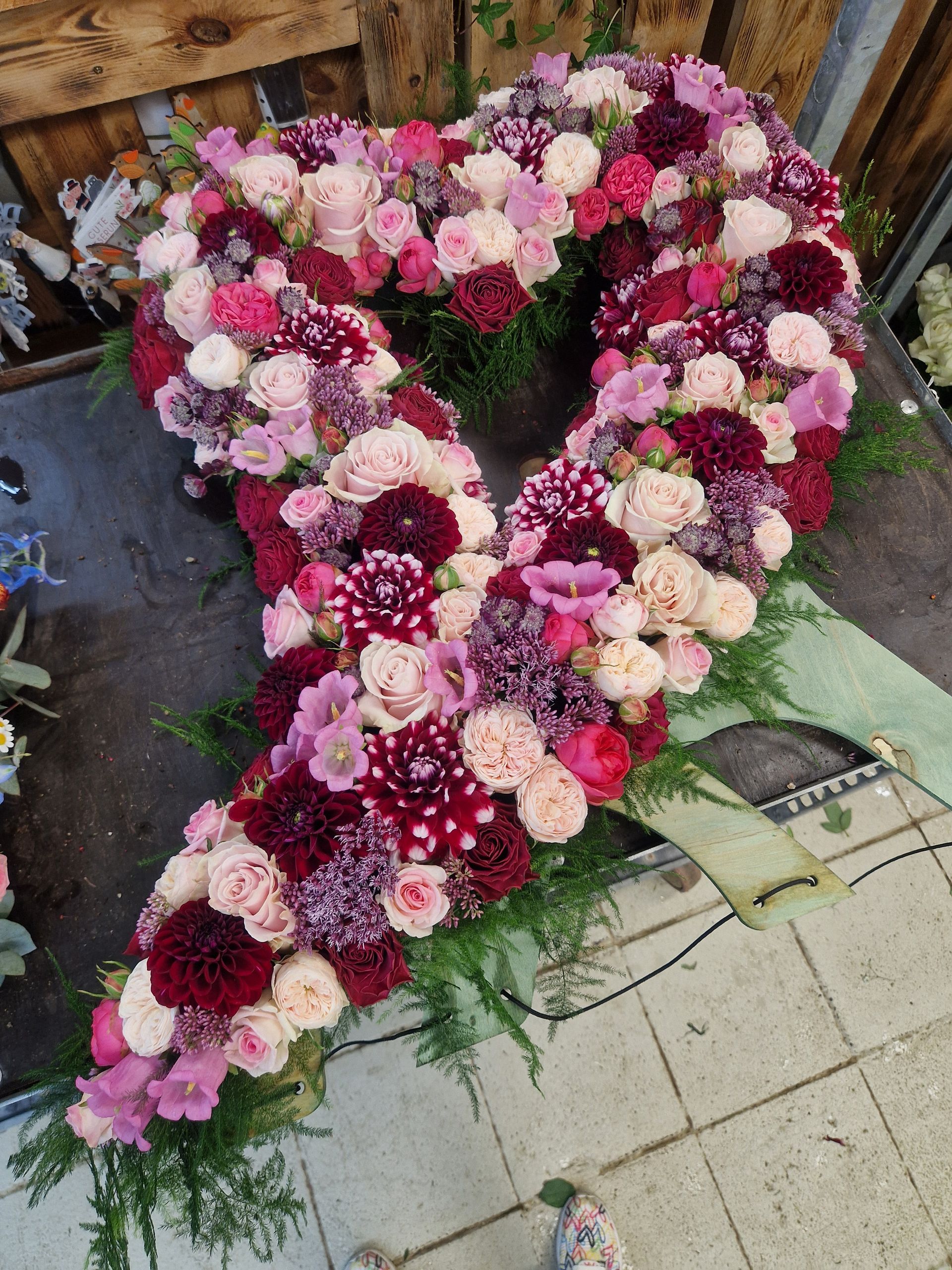 Auf einem Tisch liegt ein Herz aus rosa und roten Blumen.