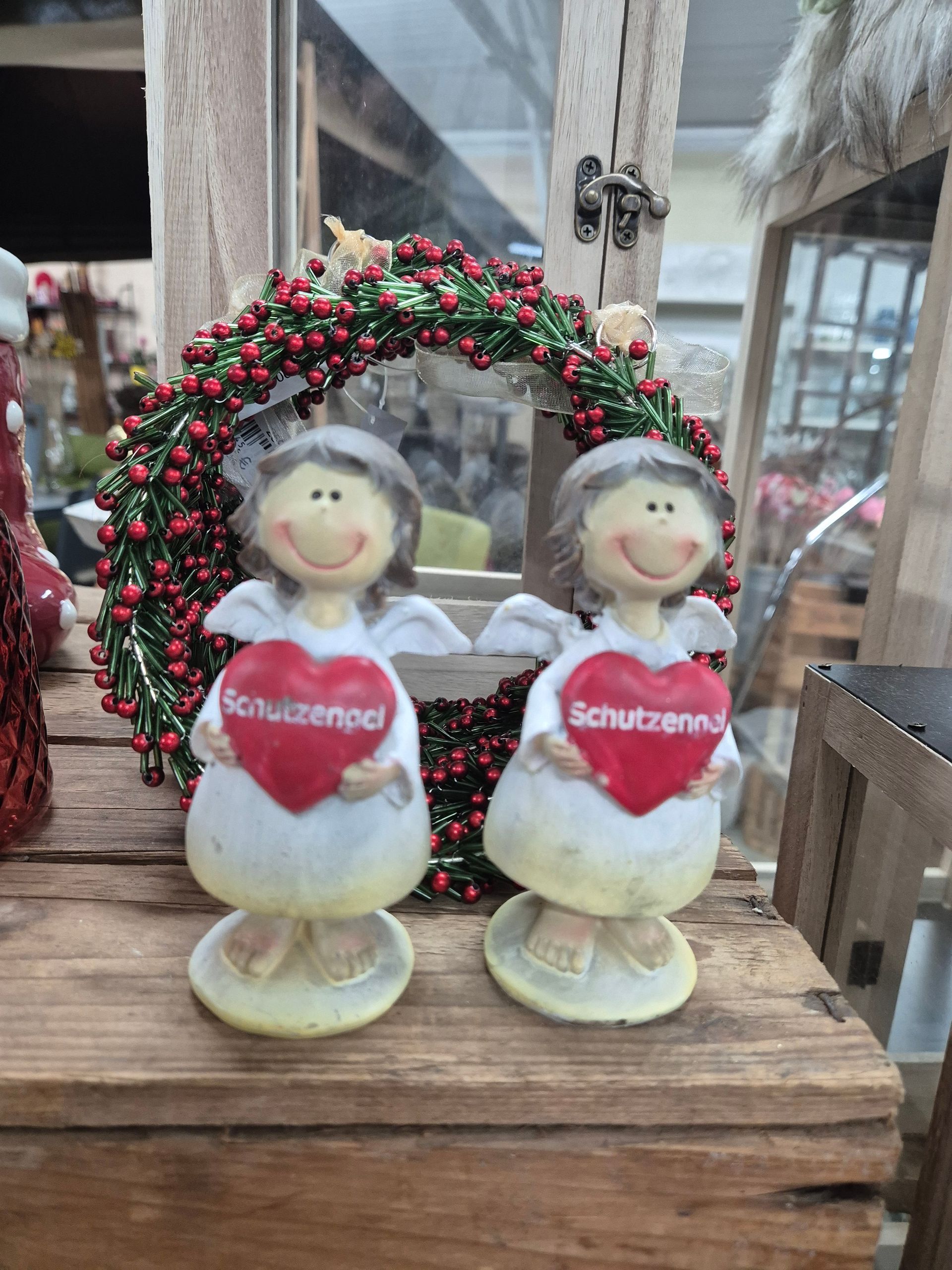 Zwei Engelfiguren, die Herzen halten, sitzen auf einem Holztisch.