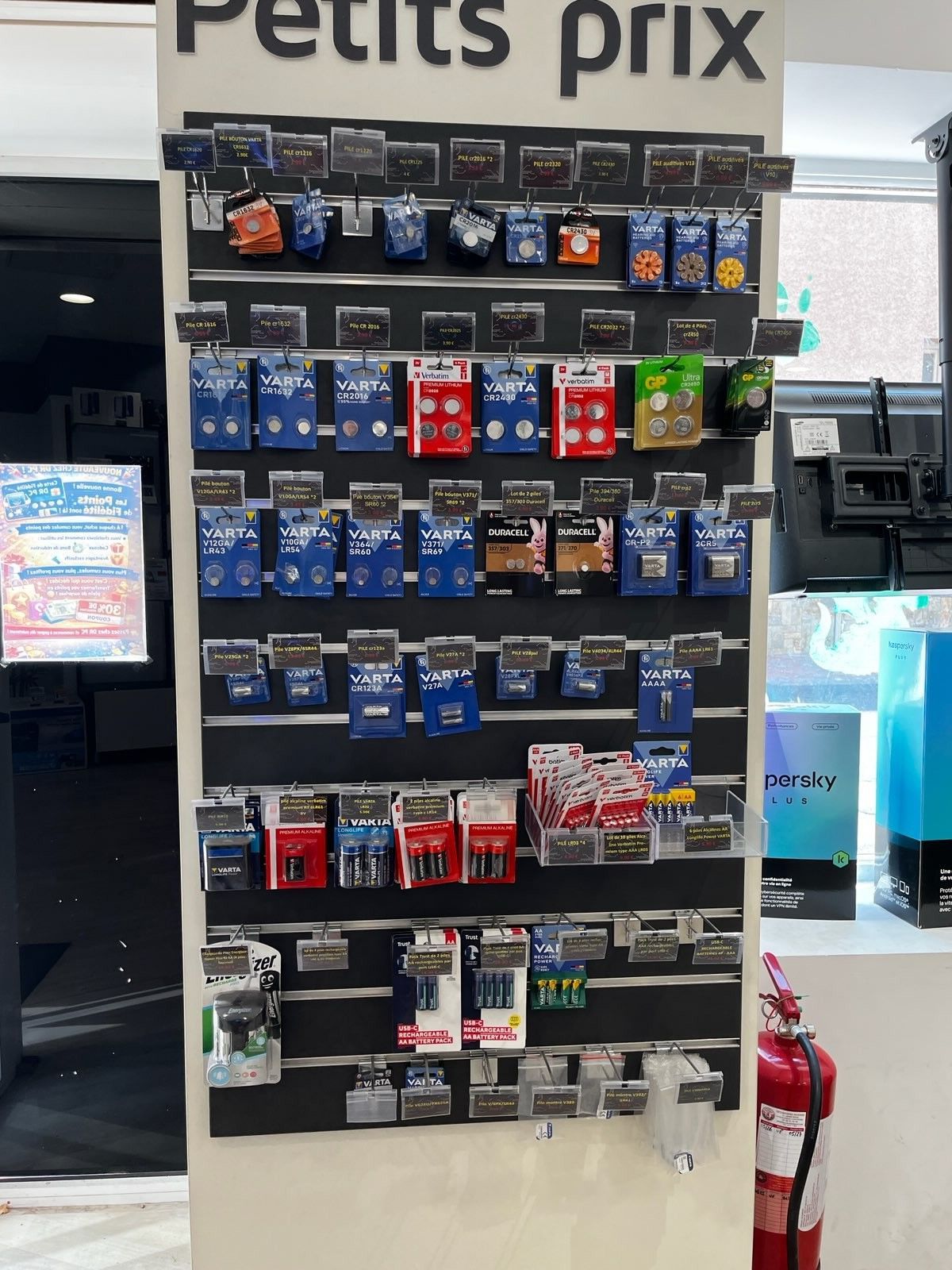 Présentoir de friandises pour animaux de compagnie en français dans un magasin, avec des articles emballés colorés assortis et une pancarte « Petits prix ».