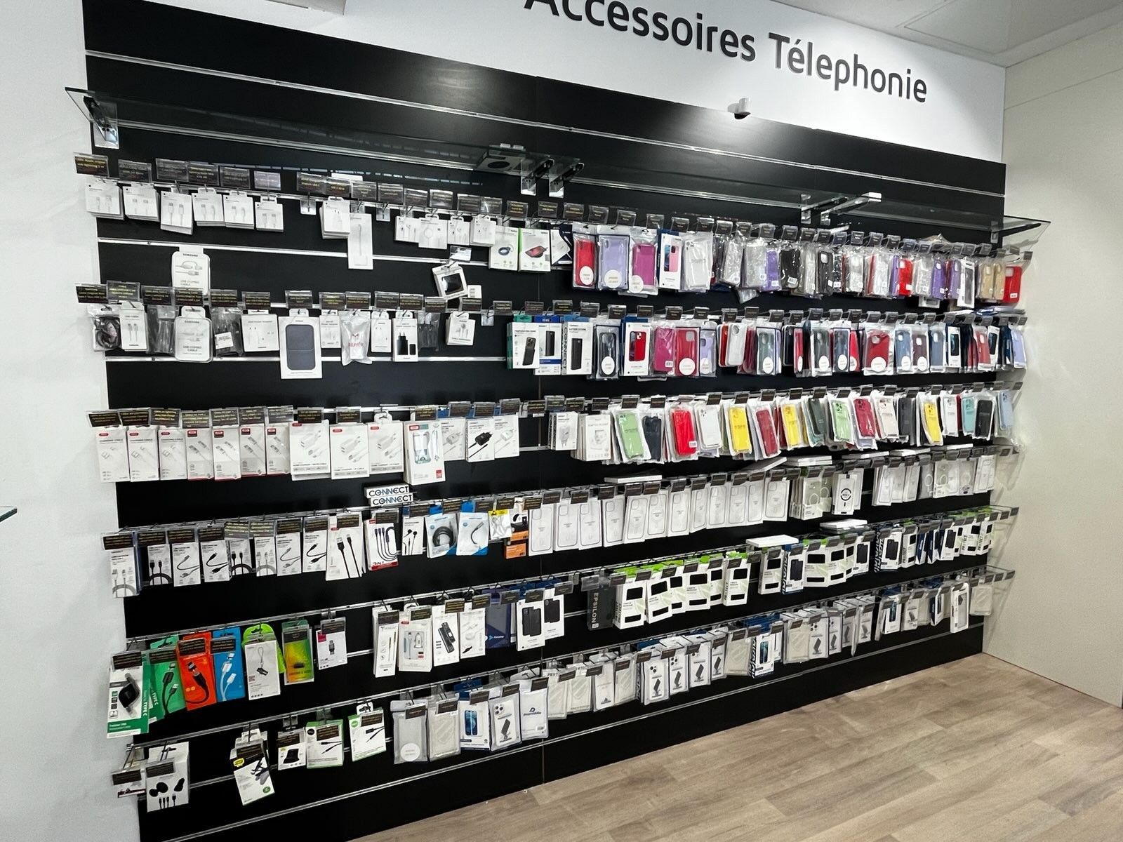 Accessoires pour téléphones présentés sur une étagère murale noire dans une allée d'un magasin.