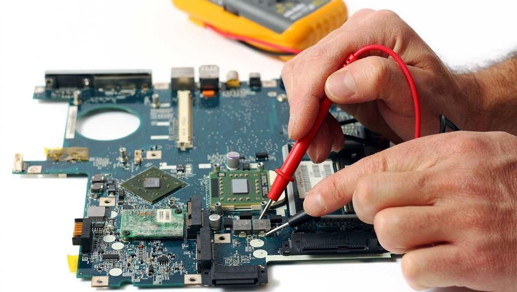 Des mains utilisent une sonde rouge pour tester la carte mère d'un ordinateur portable sur un établi.