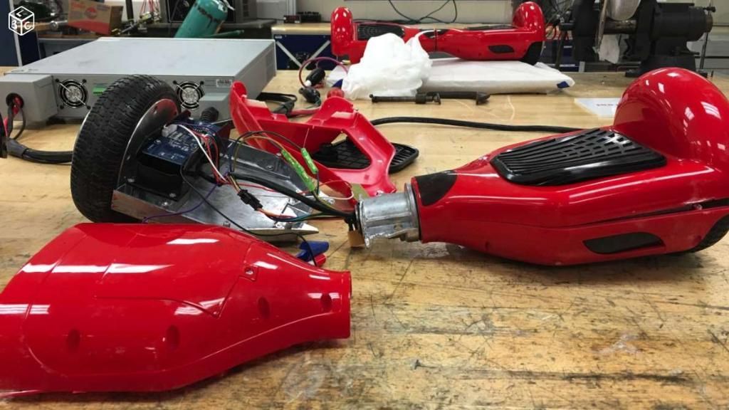 Des pièces de hoverboard rouge éparpillées sur un établi dans un atelier, roues et câbles apparents.
