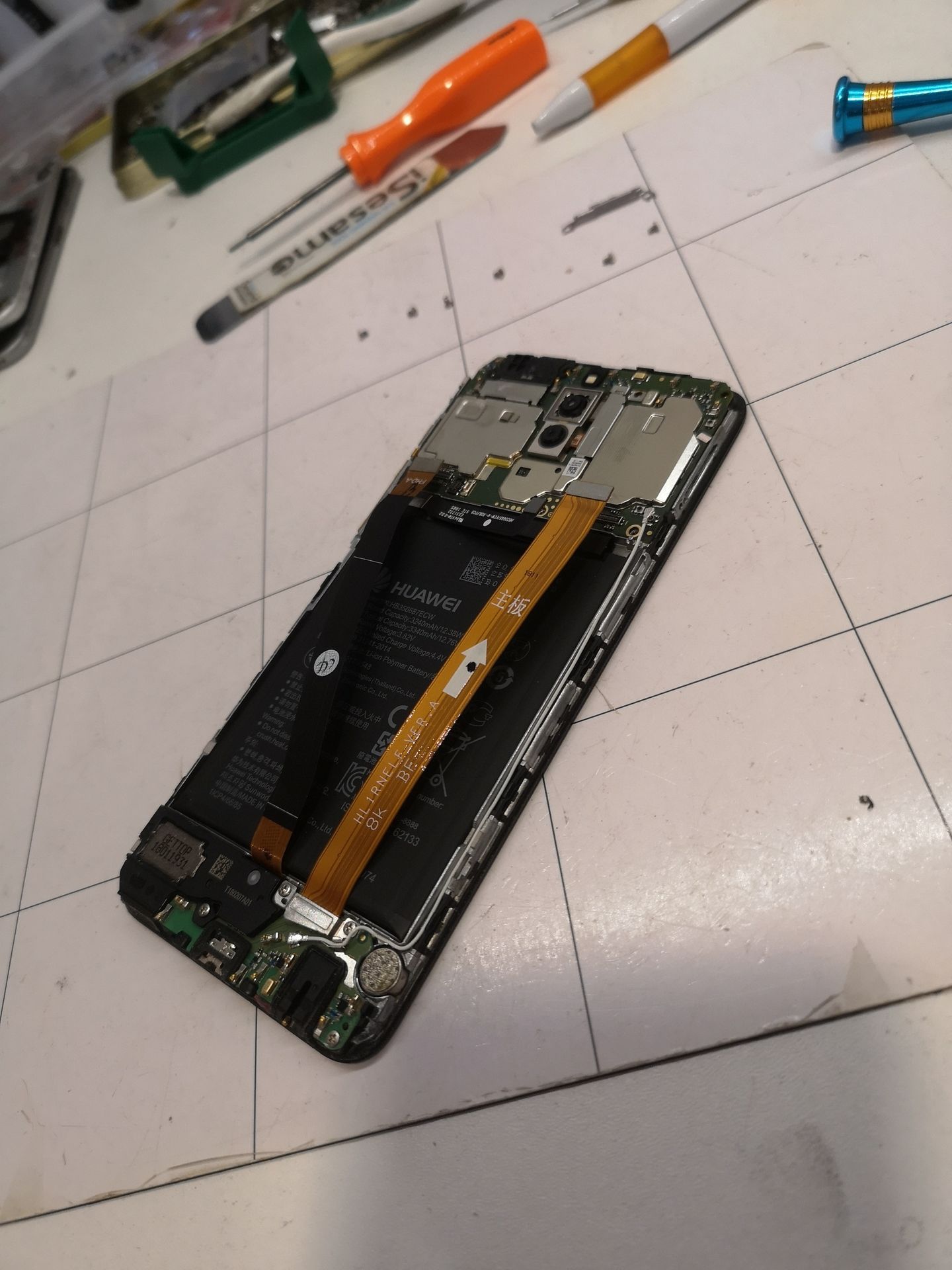 Smartphone démonté sur un établi blanc, des outils éparpillés autour.
