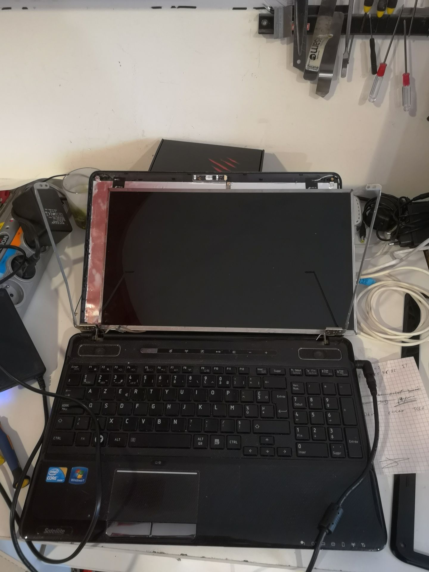 Ordinateur portable ouvert sur un bureau, écran noir, câbles et outils dans un atelier
