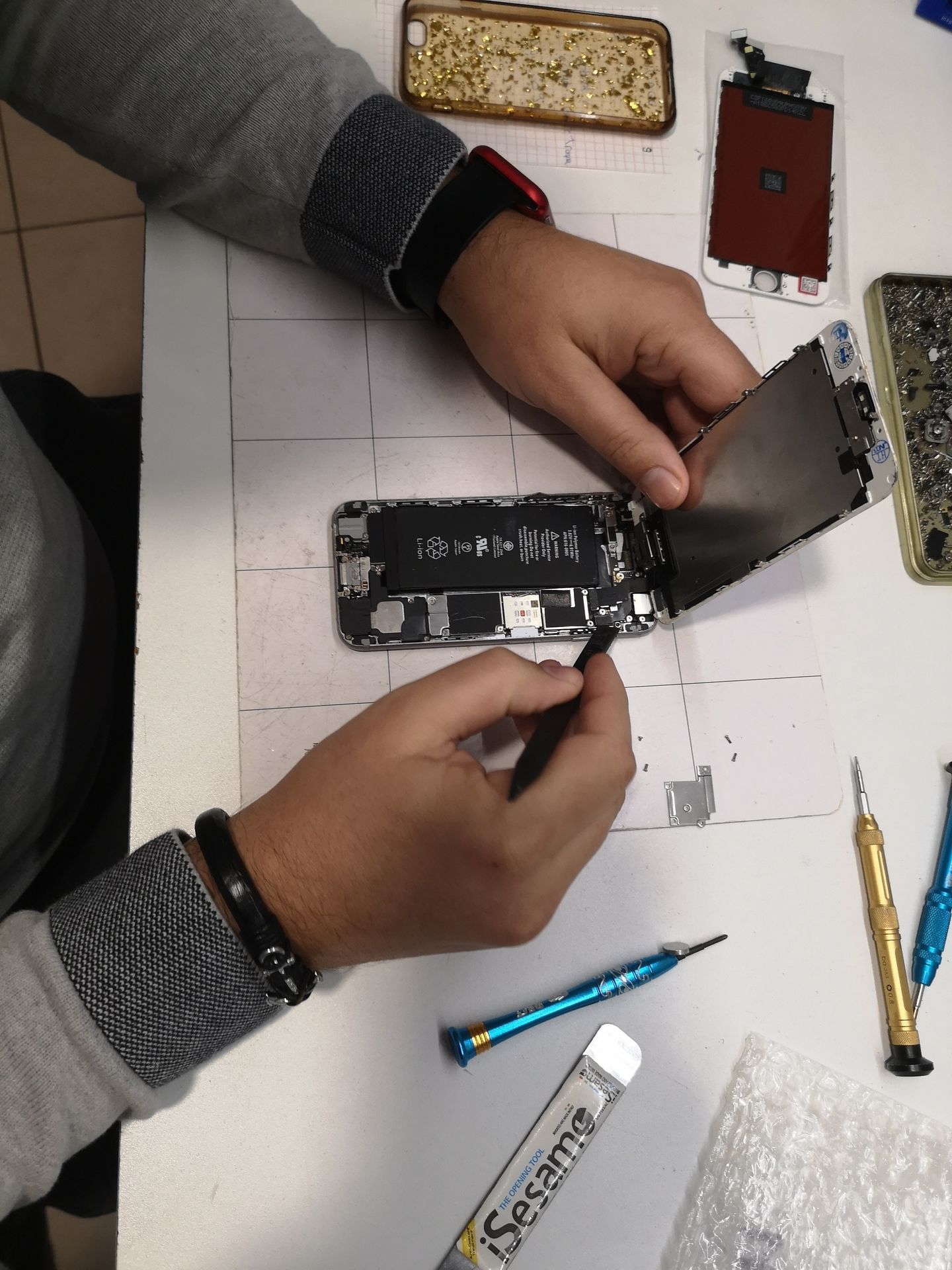 Des mains réparent un smartphone sur un établi, avec des outils et des pièces éparpillés autour.