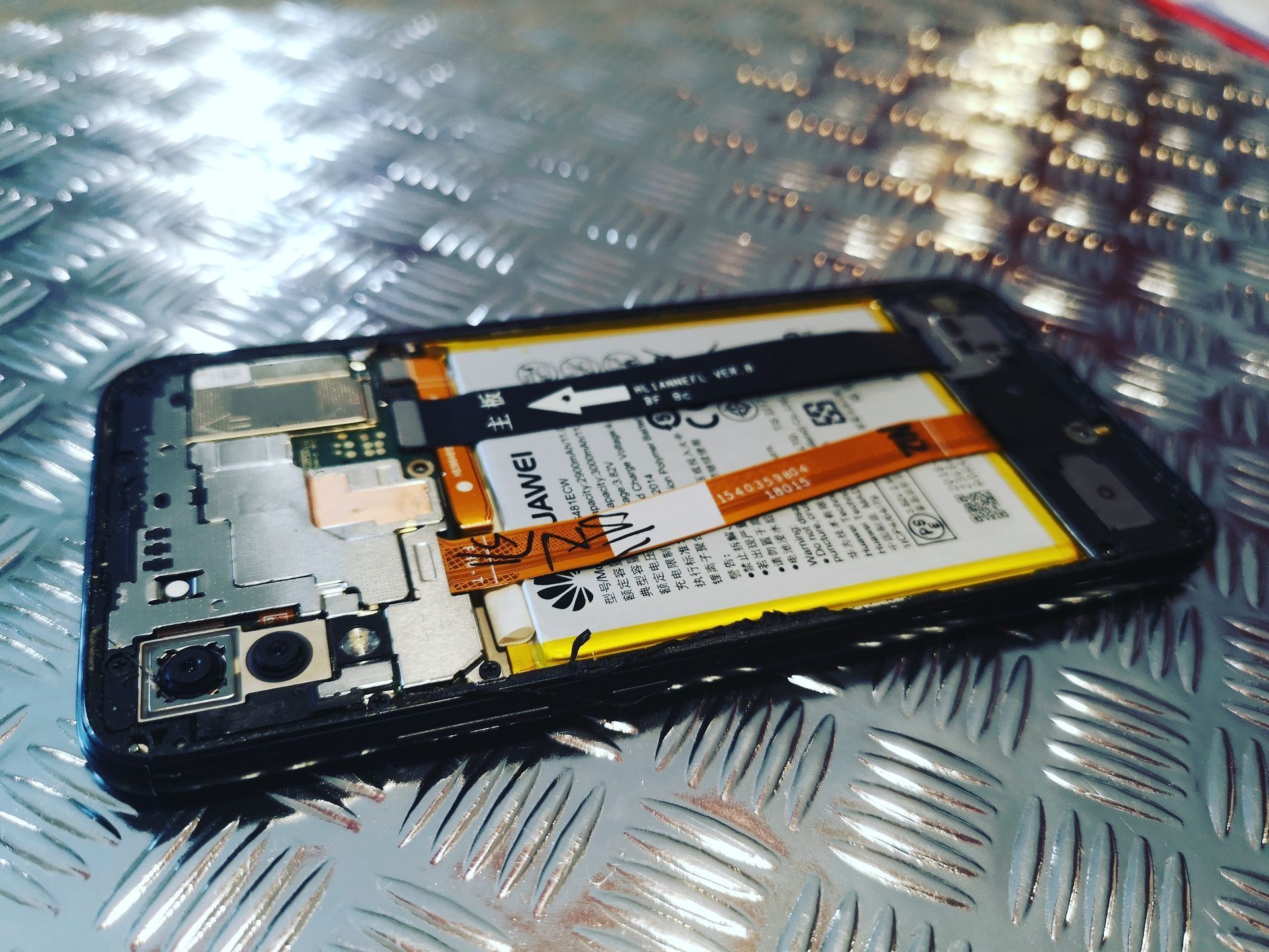 Smartphone ouvert, batterie interne et composants exposés sur une surface métallique.