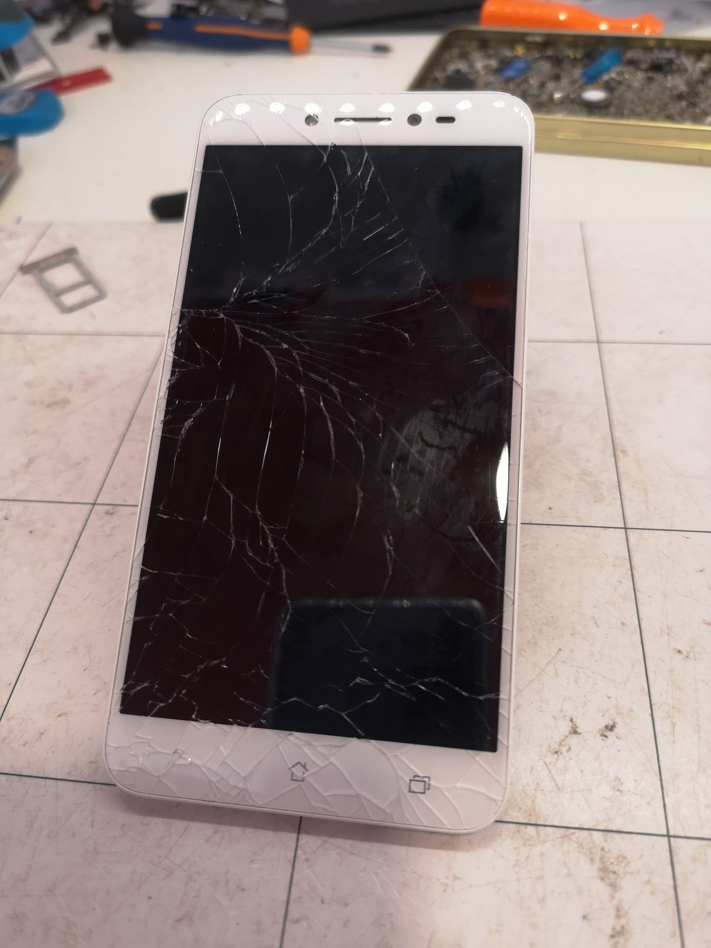 Un smartphone blanc fissuré gisant sur un établi, avec des outils en arrière-plan.