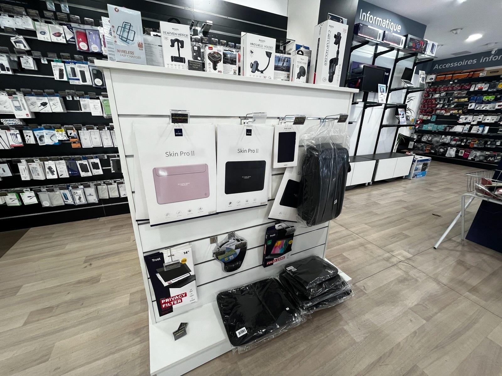 Allée d'un magasin d'électronique avec des présentoirs blancs d'étuis et d'accessoires pour téléphones, ainsi que des articles emballés au sol.