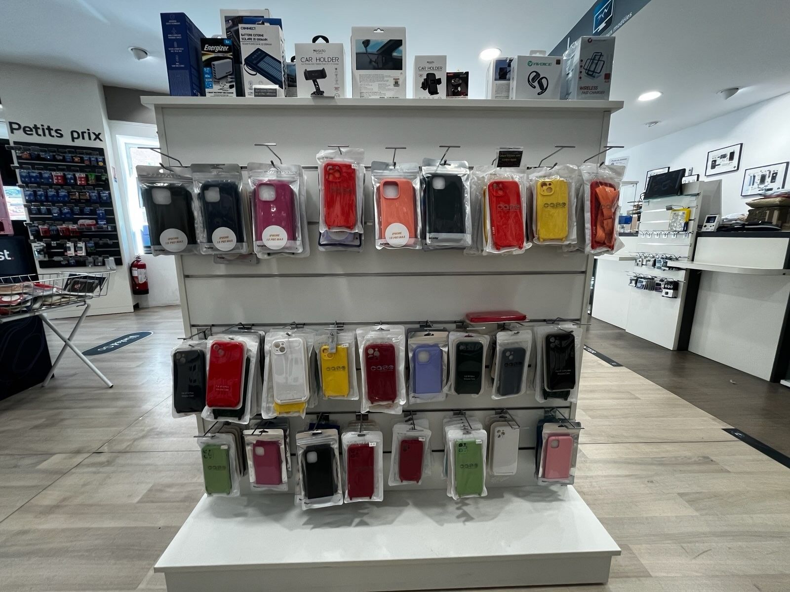 Des étuis de téléphone présentés sur des étagères blanches dans un magasin, avec des étuis colorés disposés en rangées.