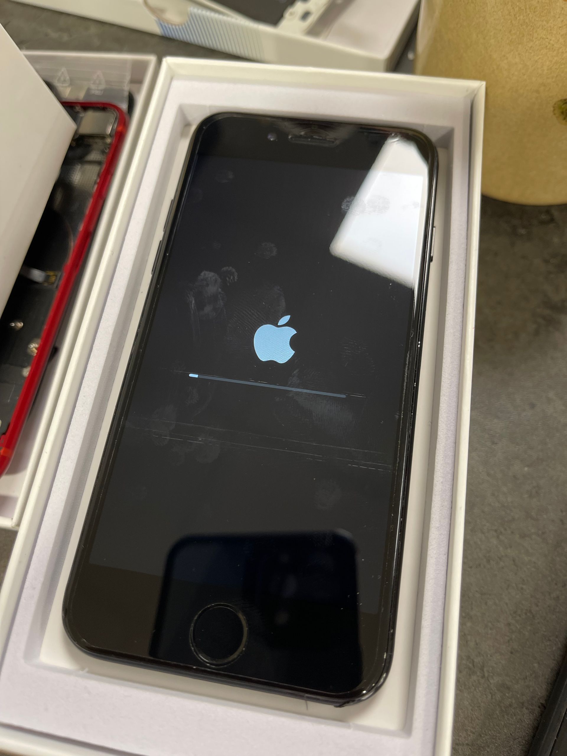 IPhone noir dans une boîte blanche affichant le logo Apple et l'écran de démarrage