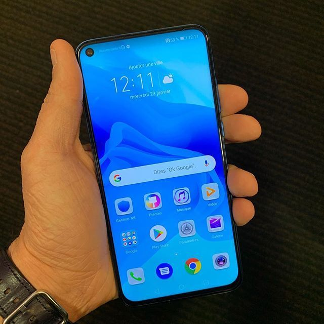 Main tenant un smartphone bleu dont l'écran d'accueil est allumé sur une surface sombre.