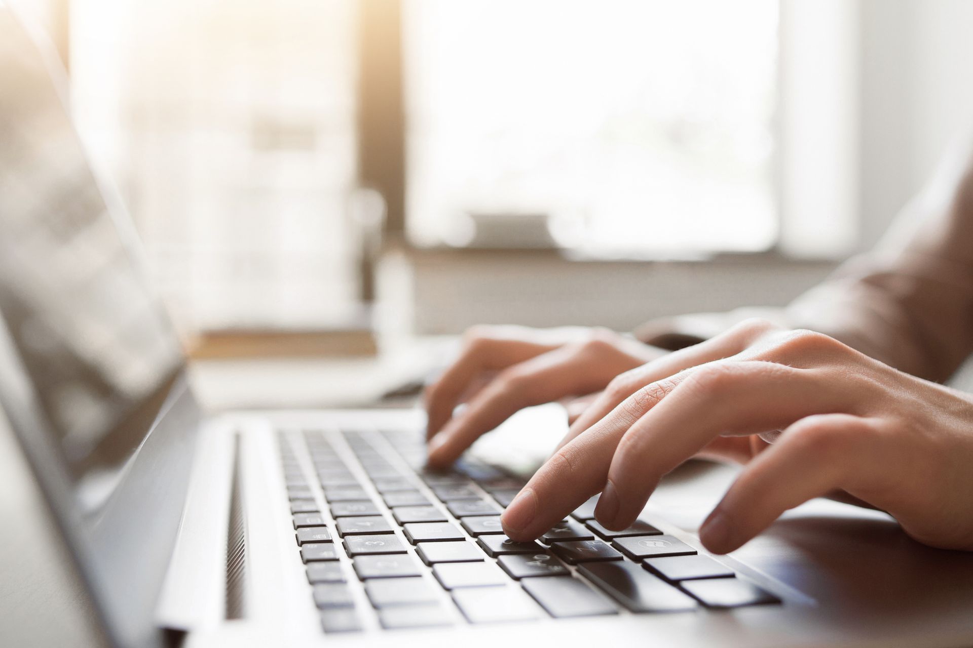 Des mains qui tapent sur un clavier d'ordinateur portable dans un environnement intérieur lumineux.