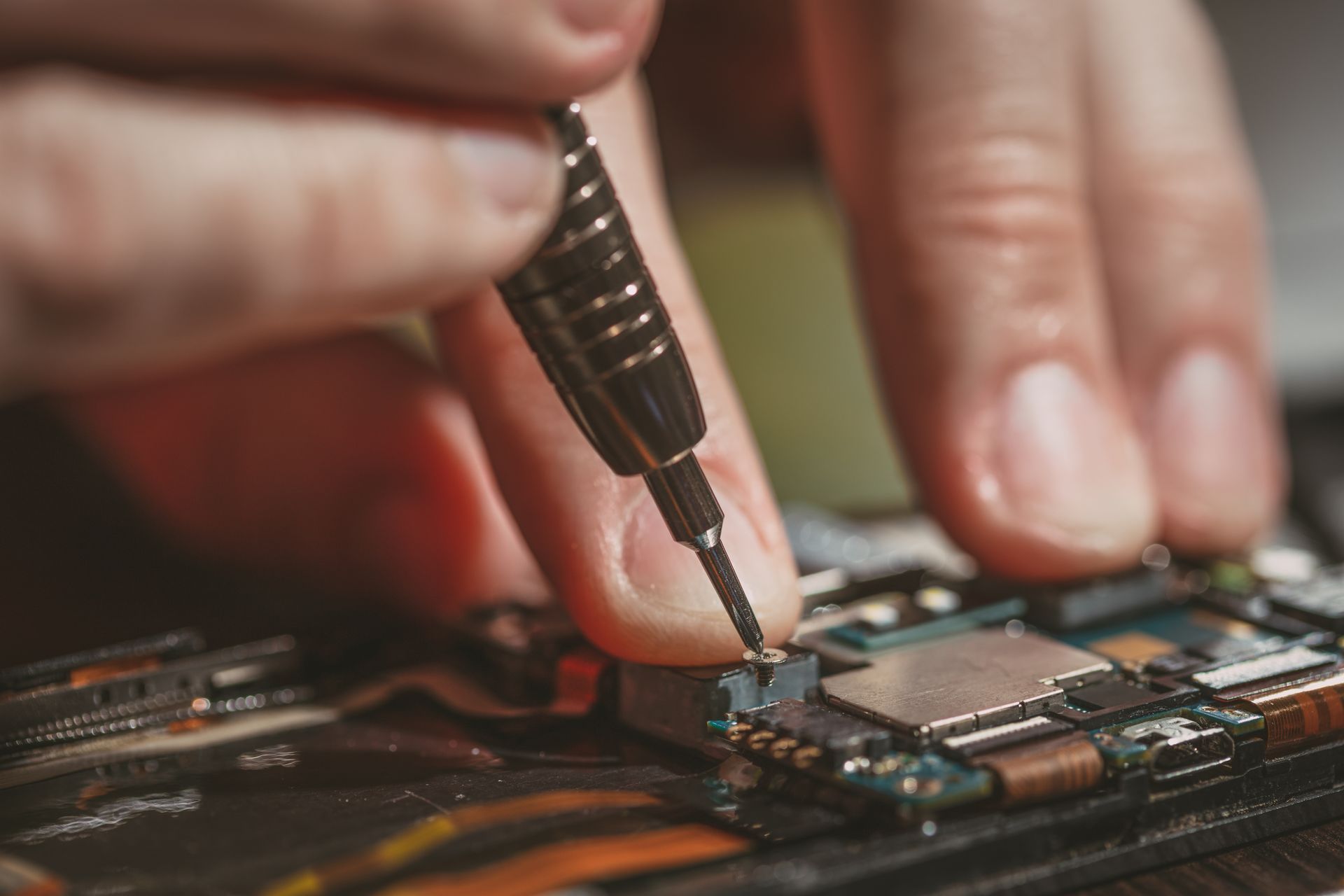 Gros plan de mains utilisant un outil de précision pour réparer une carte de circuit imprimé.