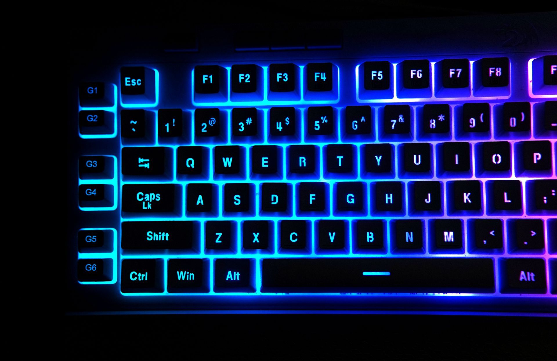 Clavier d'ordinateur rétroéclairé en bleu et violet sur fond sombre.