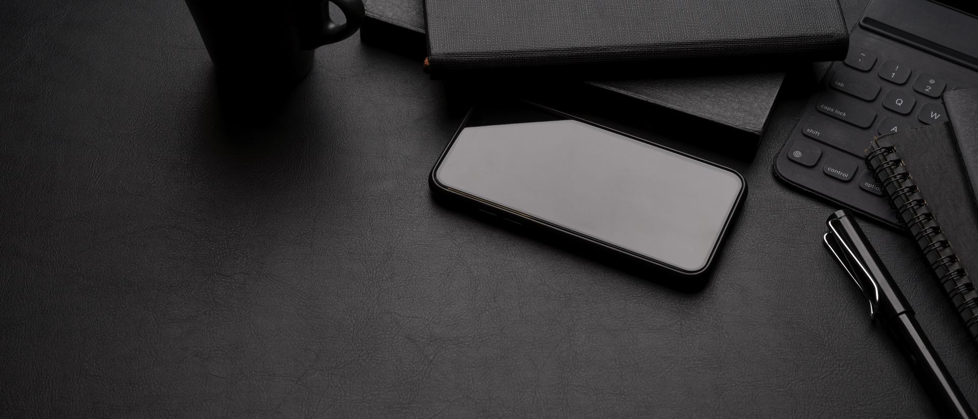 Bureau noir avec carnet, stylo, clavier et smartphone dans un espace de travail minimaliste.