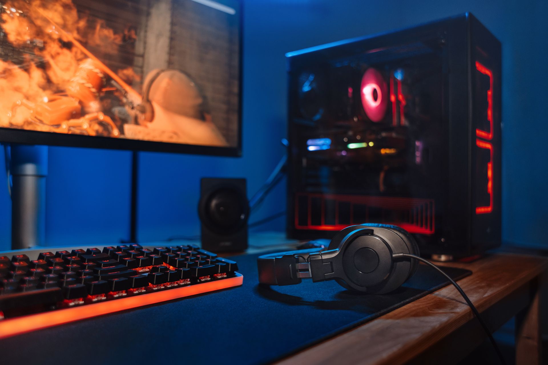 Configuration d'un bureau de jeu avec tour PC RGB, écran, clavier, souris et casque sur un bureau éclairé en bleu.