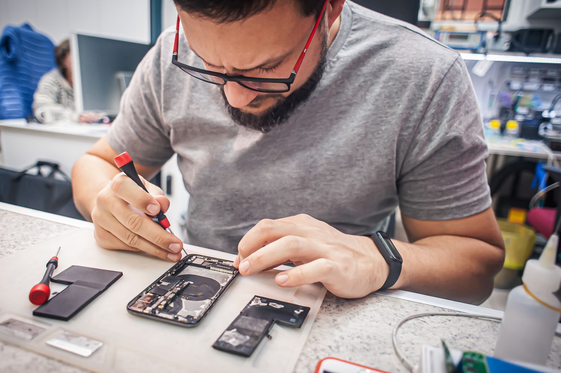 Technicien réparant un smartphone sur un établi avec des outils et des pièces détachées de téléphone.