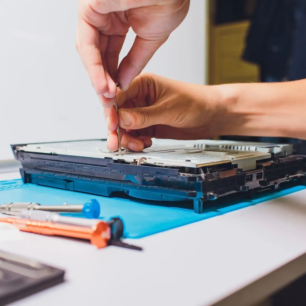 Des mains réparent les composants internes ouverts d'un ordinateur portable sur un établi, avec des outils à proximité.