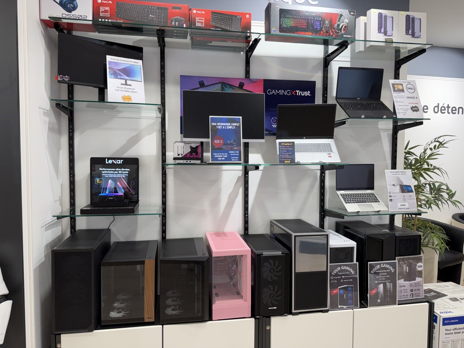 Rayonnages de magasin présentant un assortiment d'appareils électroniques et d'ordinateurs portables en boîte, sur des étagères en métal noir.