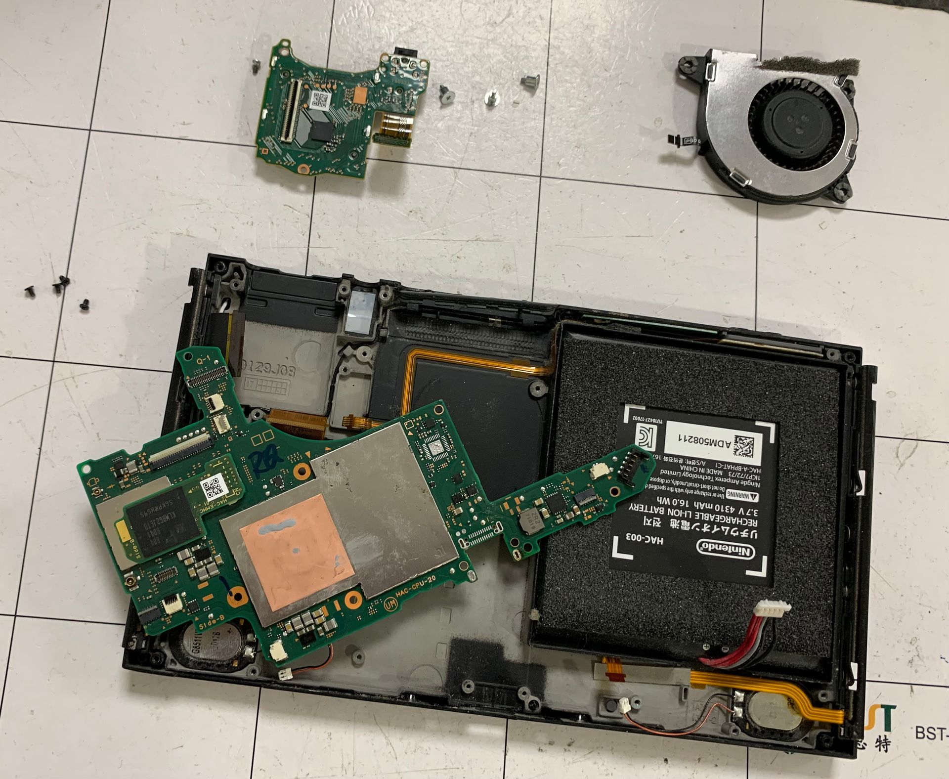 Pièces d'ordinateur portable démontées sur une surface carrelée blanche, notamment carte mère, ventilateur, batterie et petites cartes de circuits imprimés