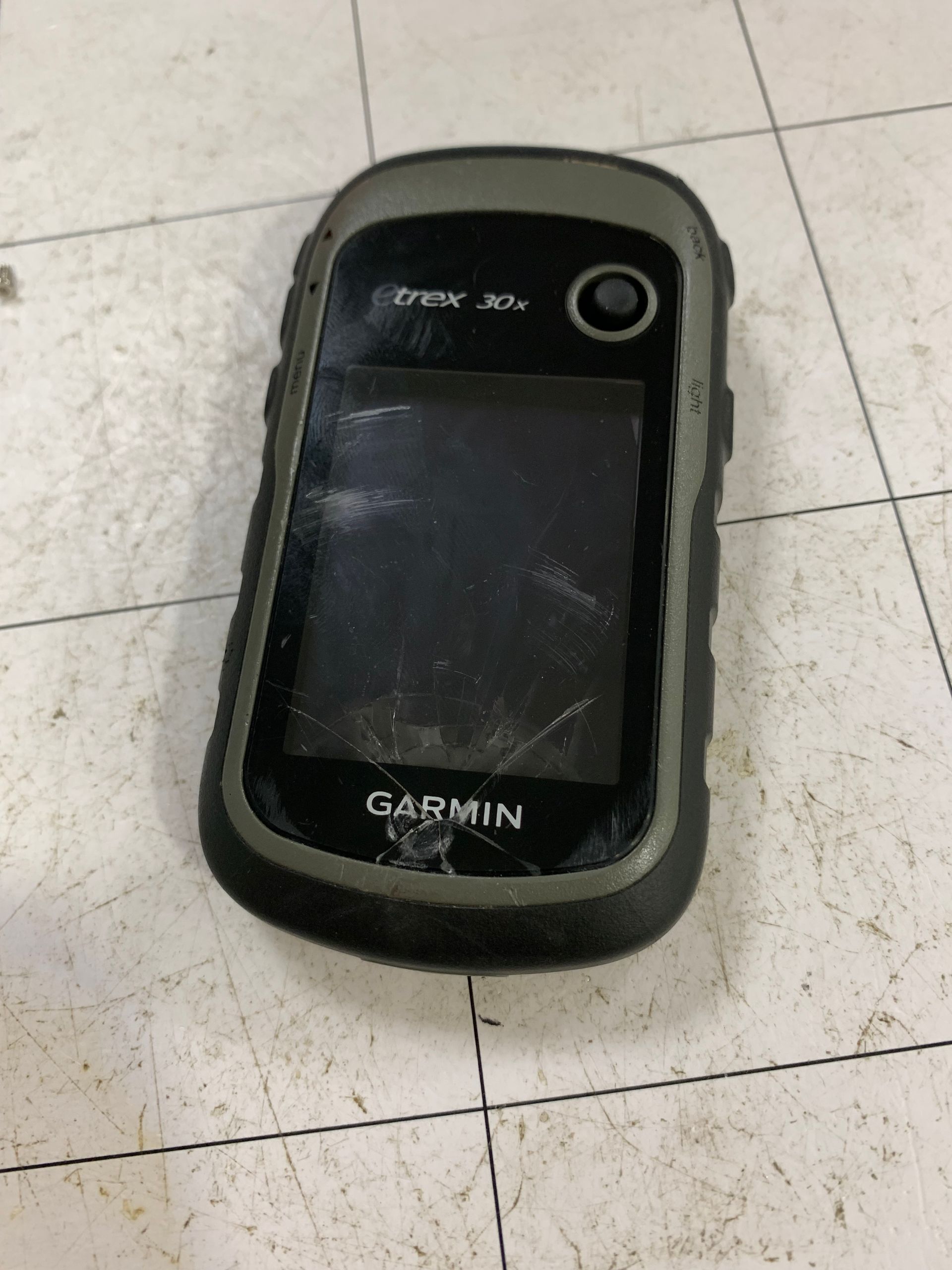 Appareil GPS Garmin noir posé sur un sol carrelé.