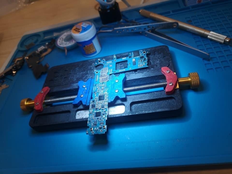 Une carte de circuit imprimé bleue fixée dans un étau sur un établi, avec des outils et des fournitures de soudure à proximité.