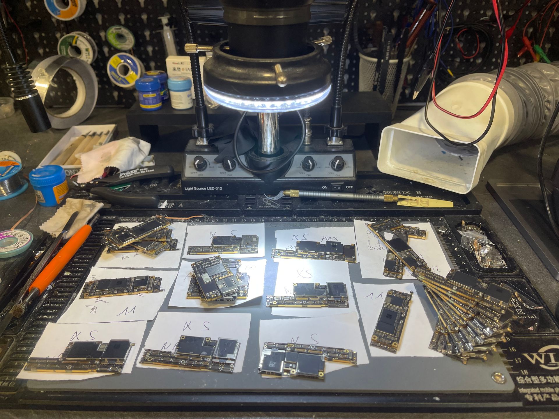 Espace de travail pour microscope avec des cartes de circuits imprimés éparpillées sur un tapis blanc et des outils autour.