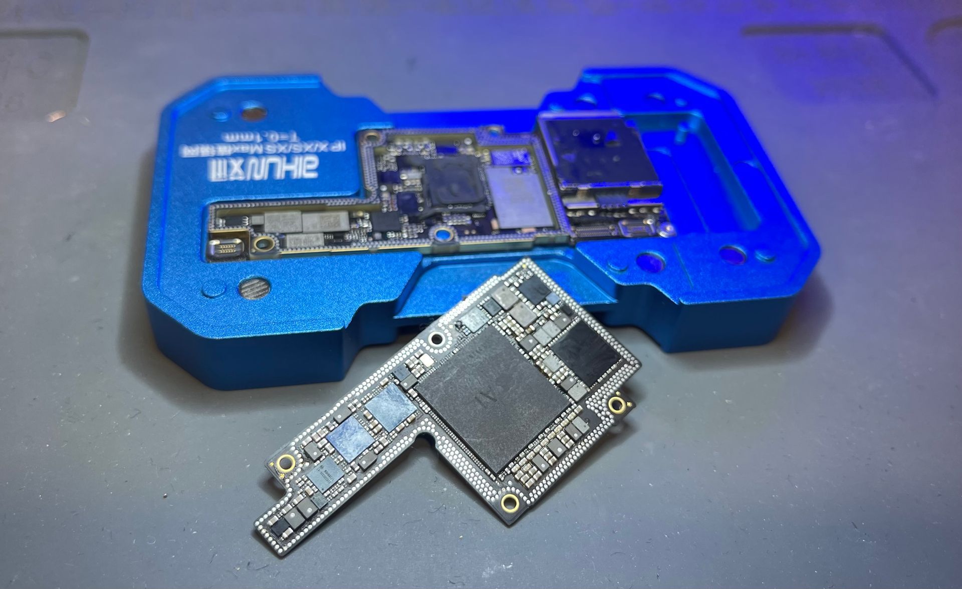 Plateau de réparation électronique bleu avec une petite carte de circuit imprimé au premier plan et un appareil démonté à l'intérieur.