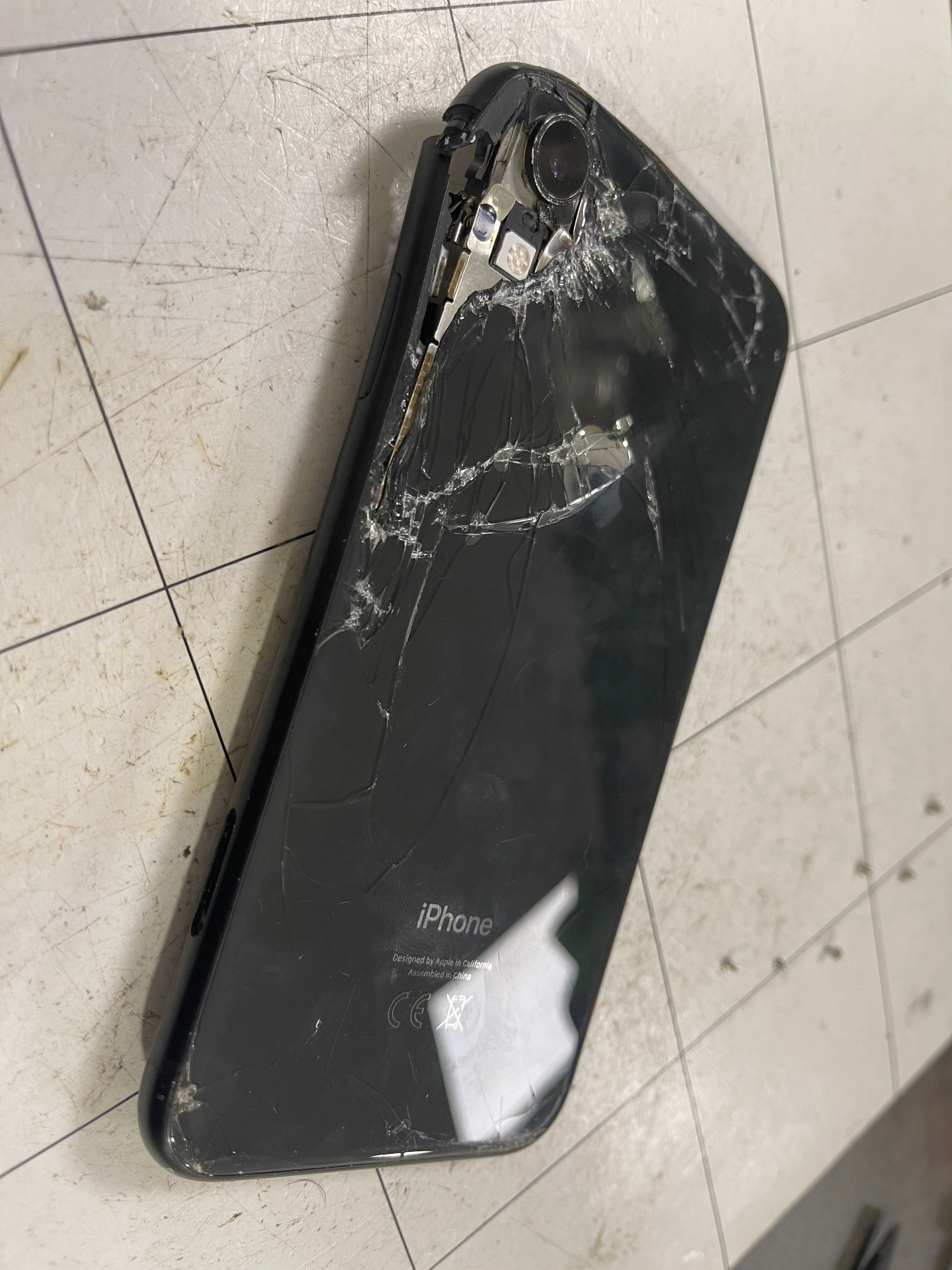 Smartphone noir fissuré posé sur un sol carrelé