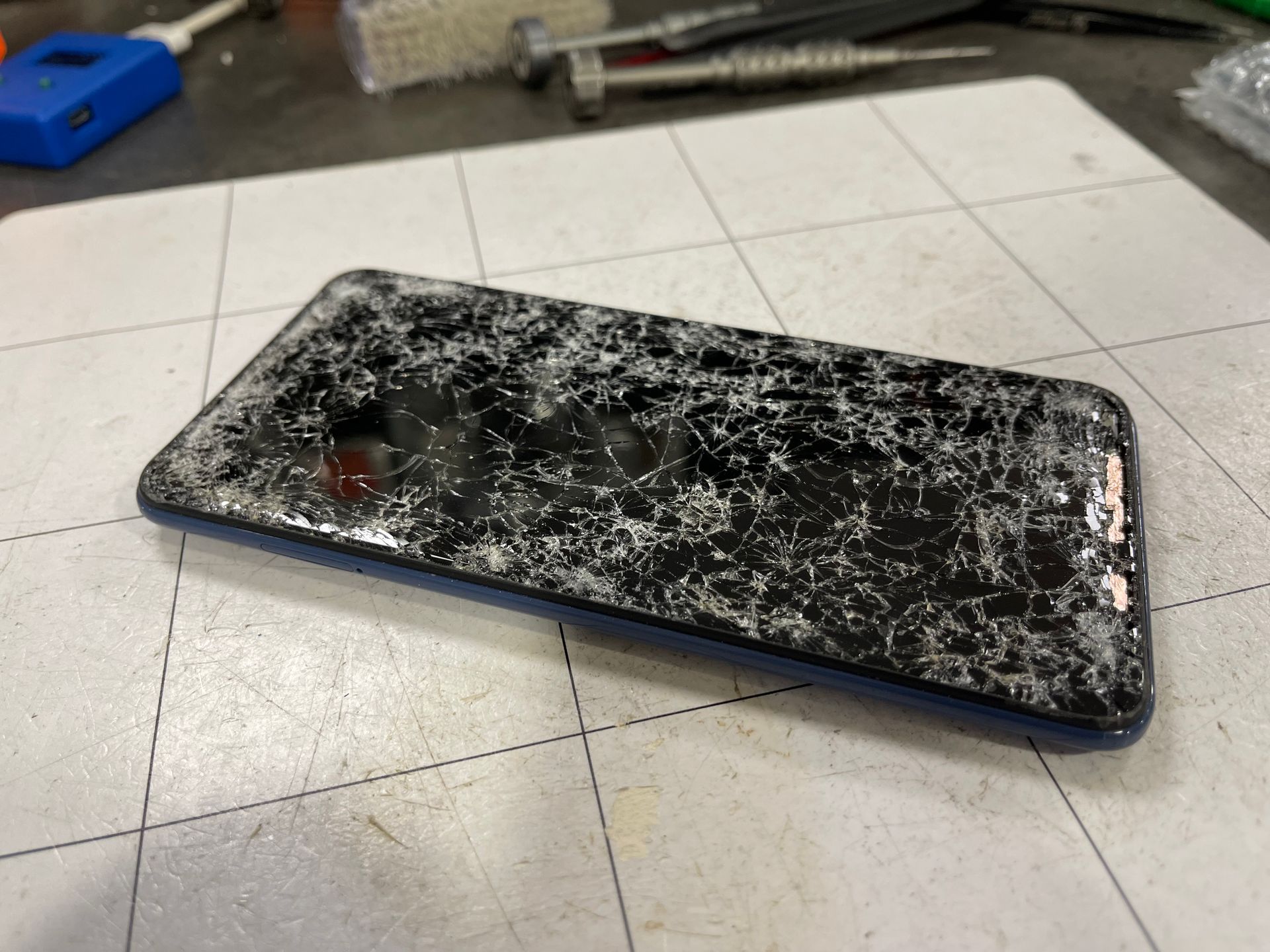 Smartphone noir fissuré, écran brisé, posé sur un établi.