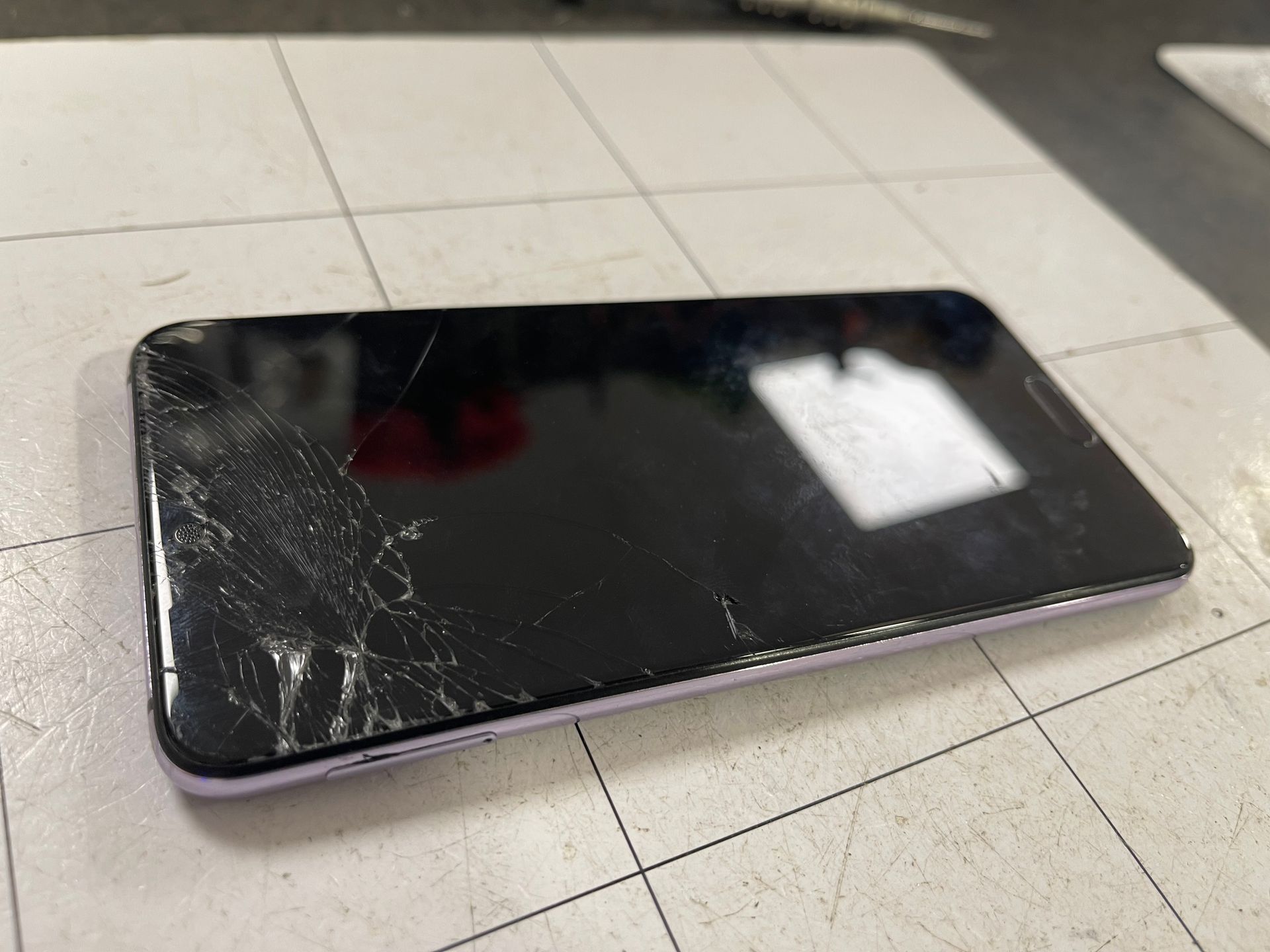 Smartphone noir fissuré posé face vers le haut sur un sol carrelé