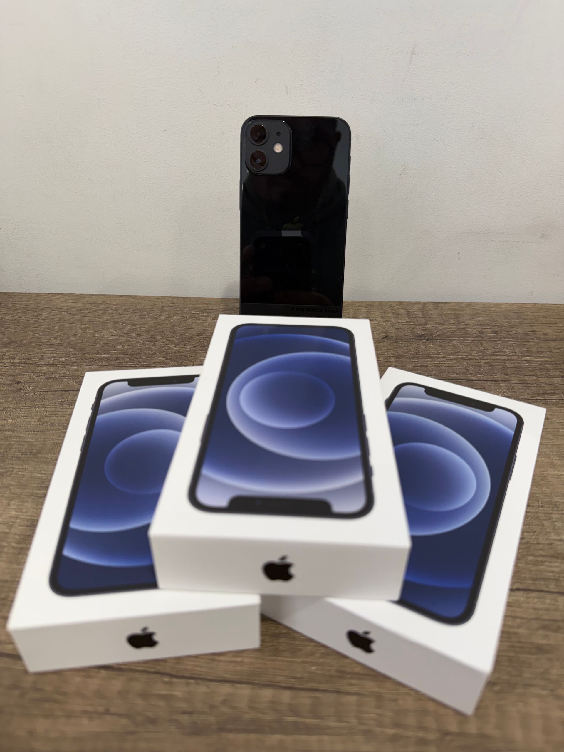 Trois boîtes blanches d'iPhone disposées devant un téléphone noir sur une surface recouverte de moquette