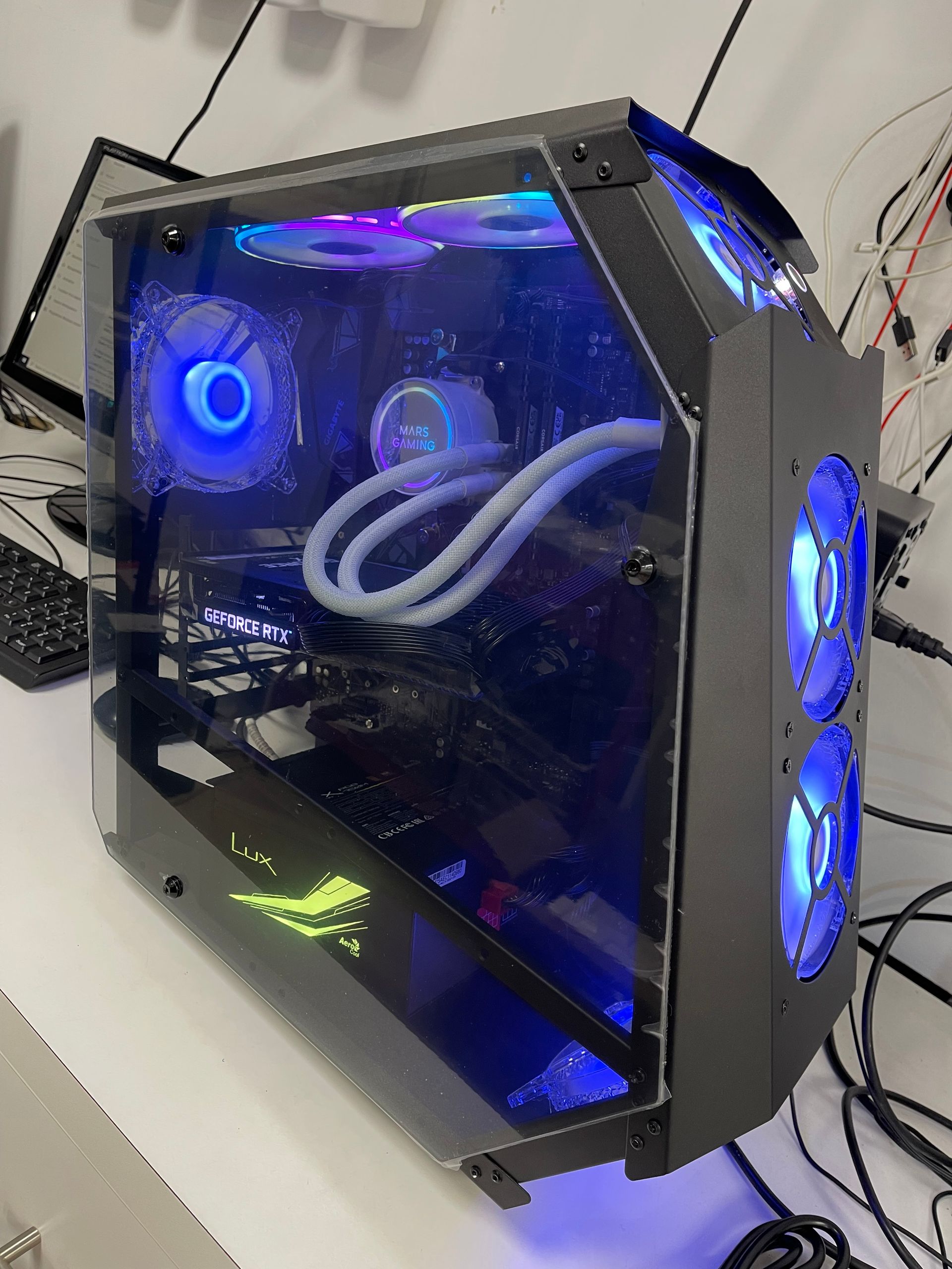 Tour PC gaming transparente avec ventilateurs rétroéclairés en bleu et tubes de refroidissement liquide blancs sur un bureau