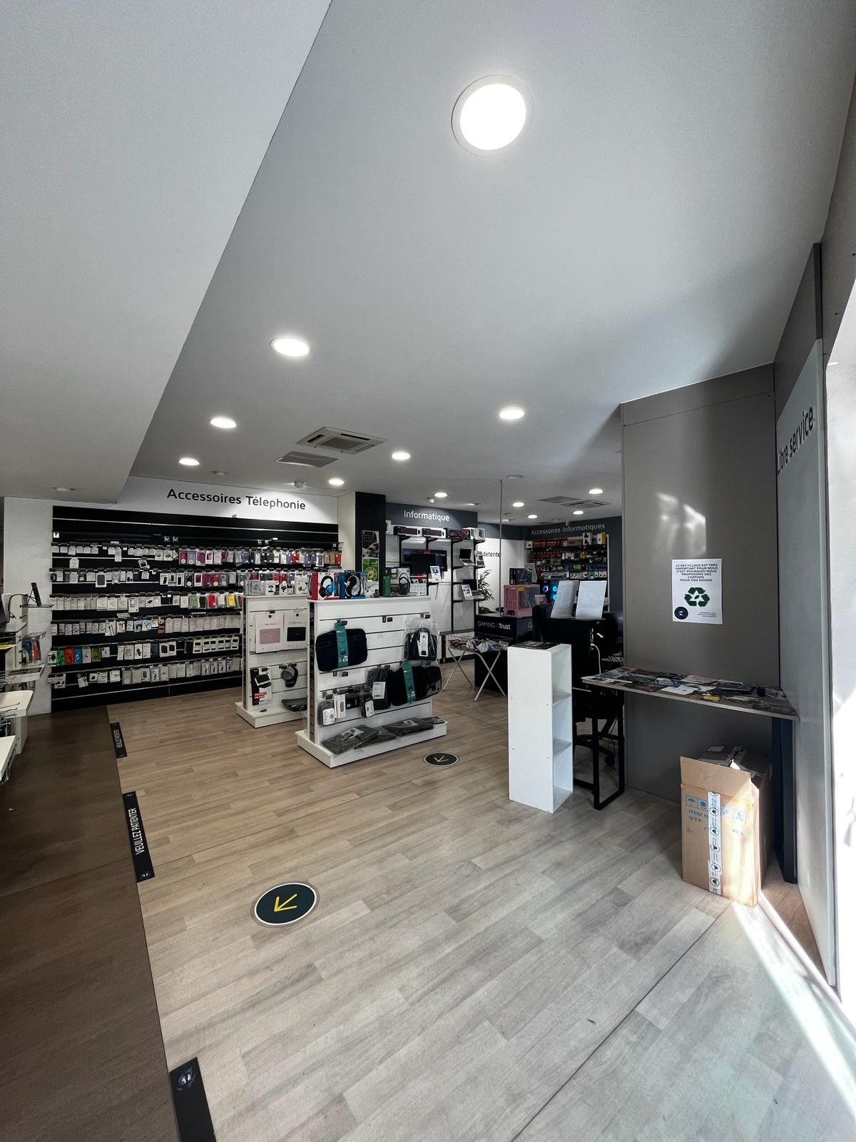 Intérieur lumineux d'un magasin avec étagères, tables d'exposition, éclairage encastré et parquet clair.