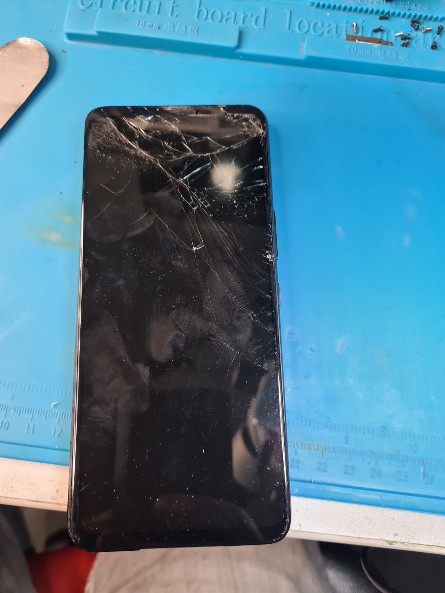 Smartphone noir fissuré posé sur un tapis de travail bleu