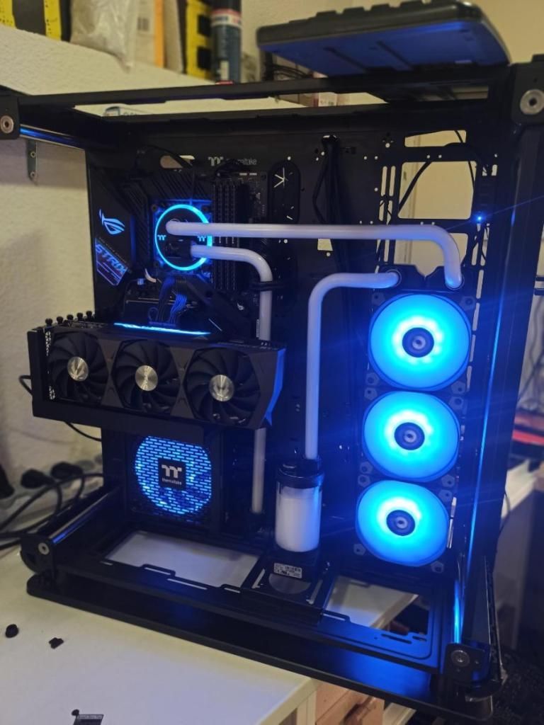 PC de bureau personnalisé avec ventilateurs rétroéclairés RGB bleus, refroidissement liquide et panneau latéral en verre, posé sur une étagère.
