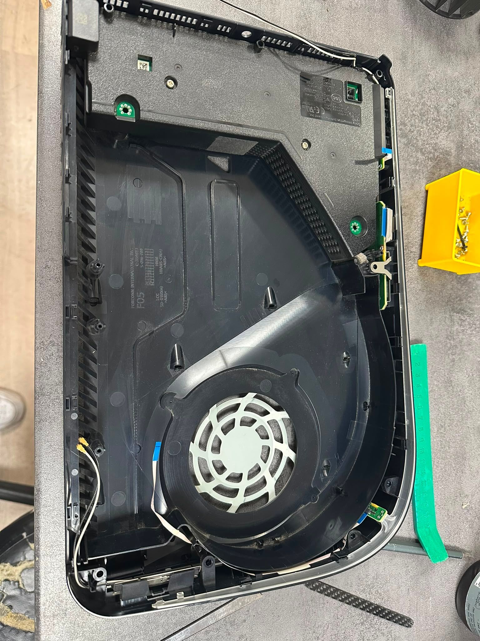 Appareil ouvert montrant un ventilateur intérieur noir et un boîtier gris, avec des étiquettes vertes sur le côté.