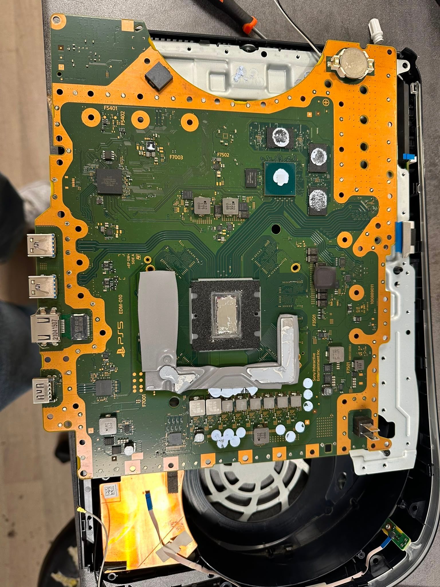 Ordinateur portable ouvert montrant la carte mère verte et le blindage orange, avec le ventilateur visible en bas à droite.