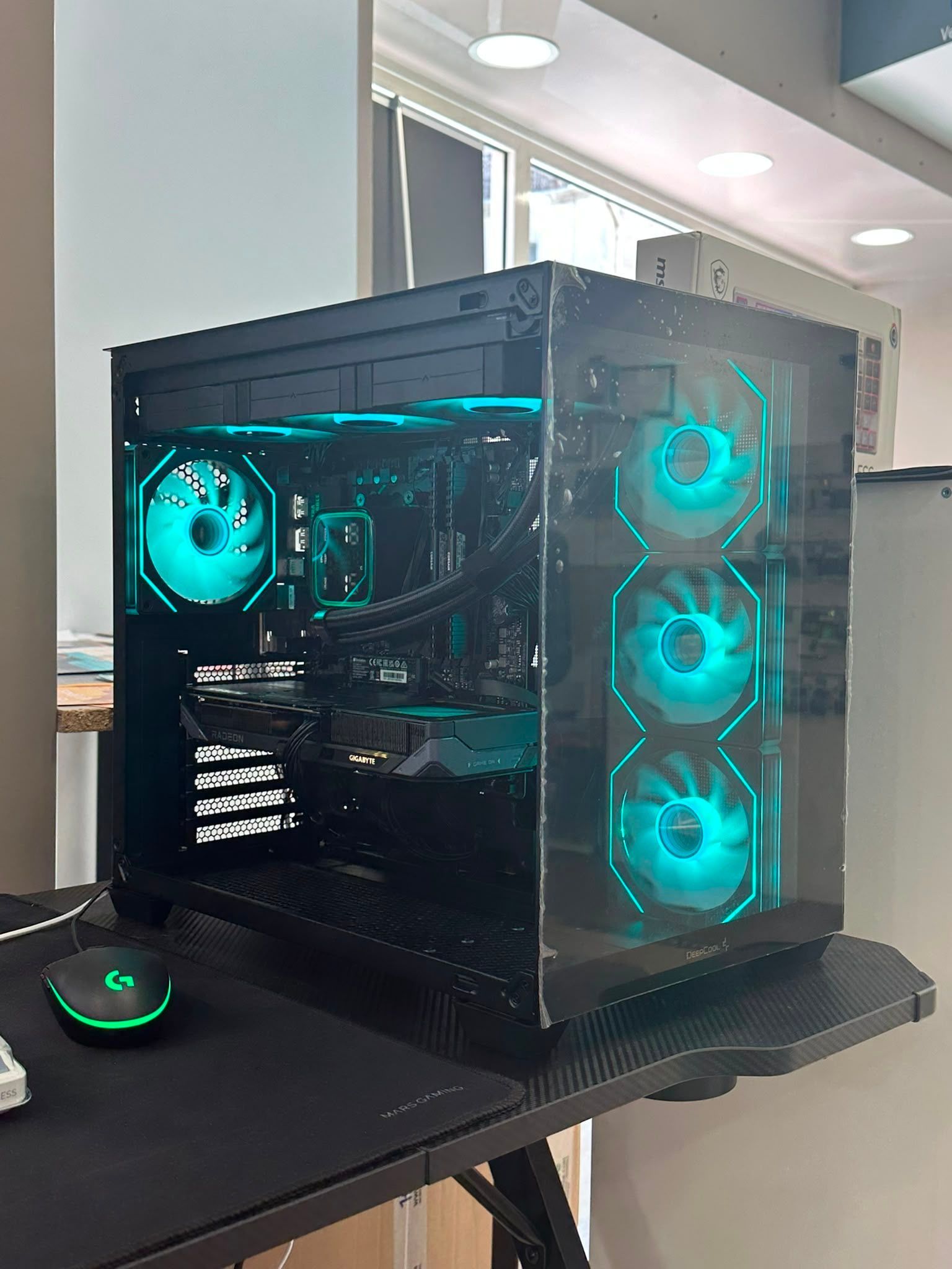 Tour PC gaming noire avec ventilateurs LED turquoise sur un bureau, à côté d'une souris sur un tapis lumineux.