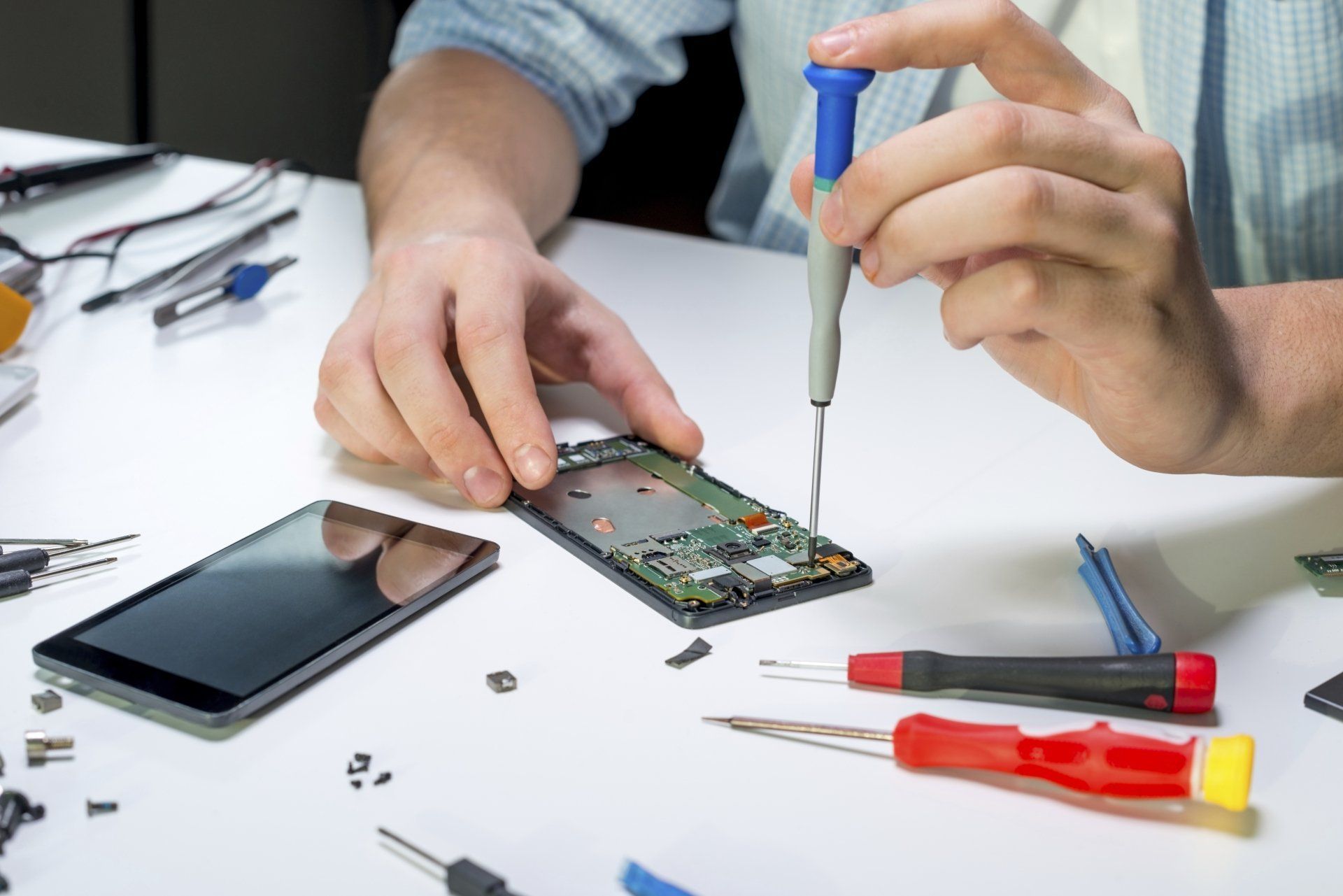 Technicien qui répare un smartphone avec des outils de précision.