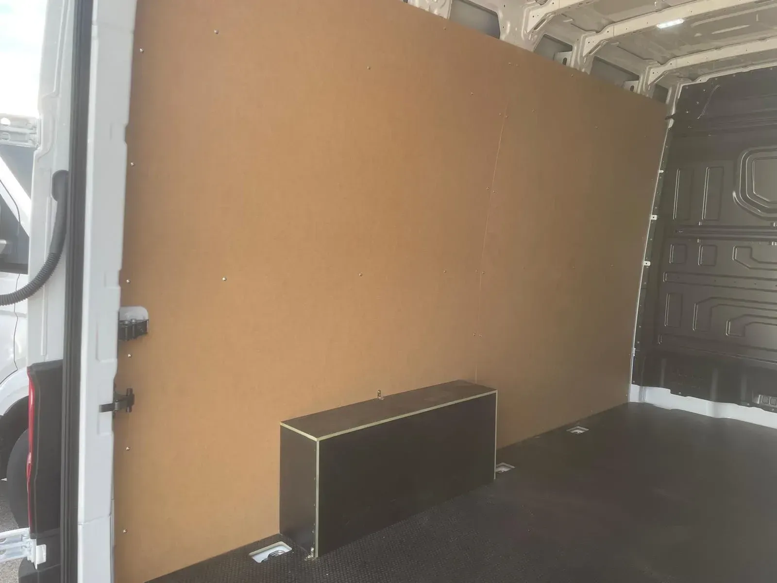 Interior de una furgoneta blanca con un gran tabique marrón y una caja de almacenamiento negra.