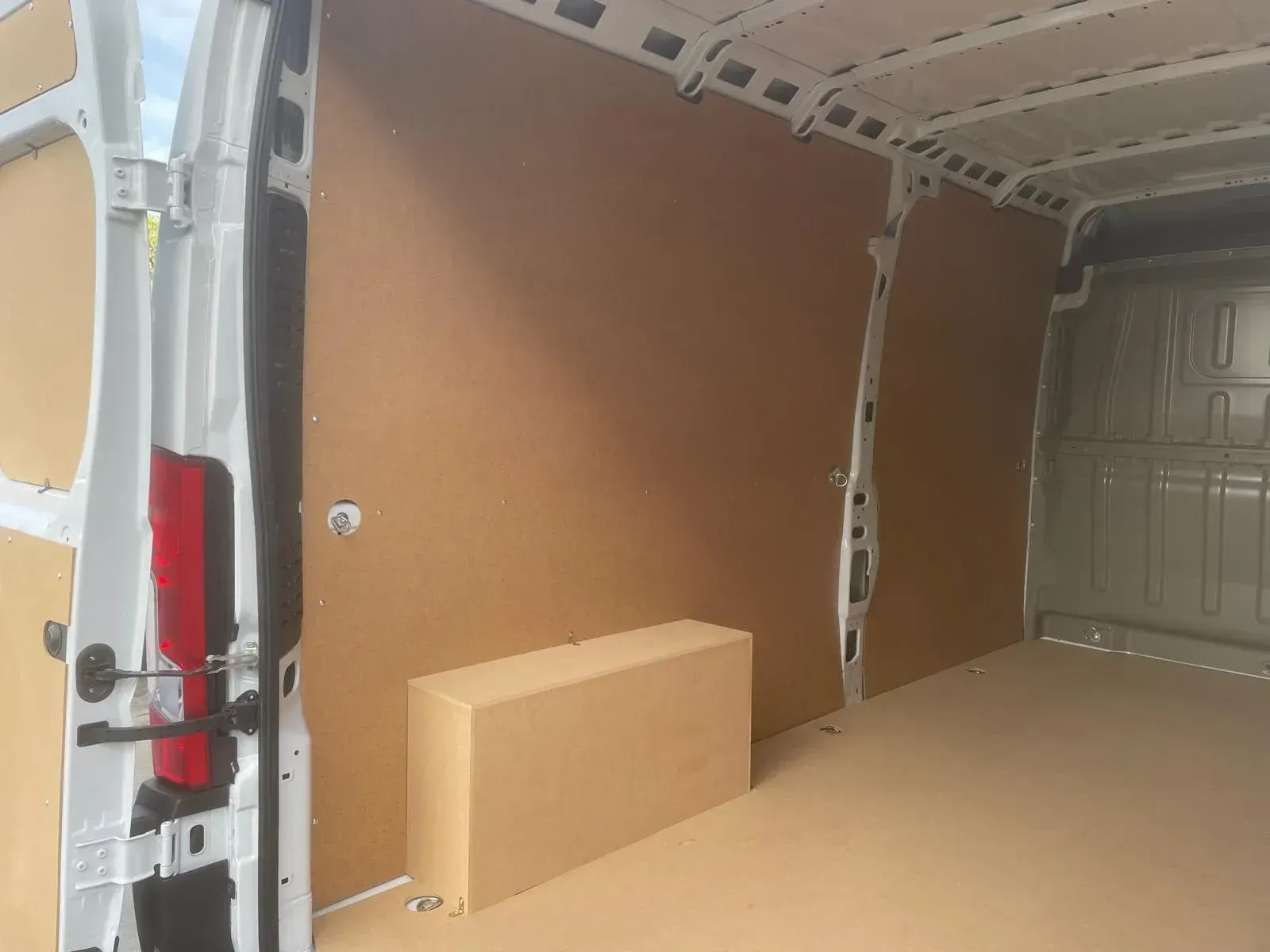 Interior de una furgoneta blanca con paneles marrones en las paredes y el suelo, y una gran caja de cartón.
